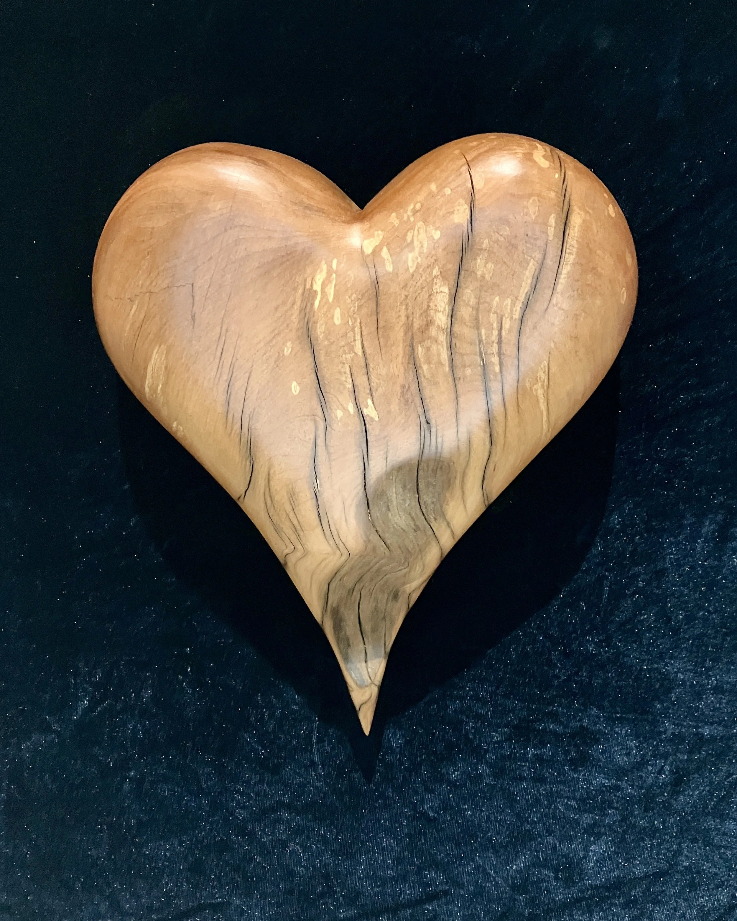 Wooden heart-shaped sculpture with natural wood grain pattern on a black surface.