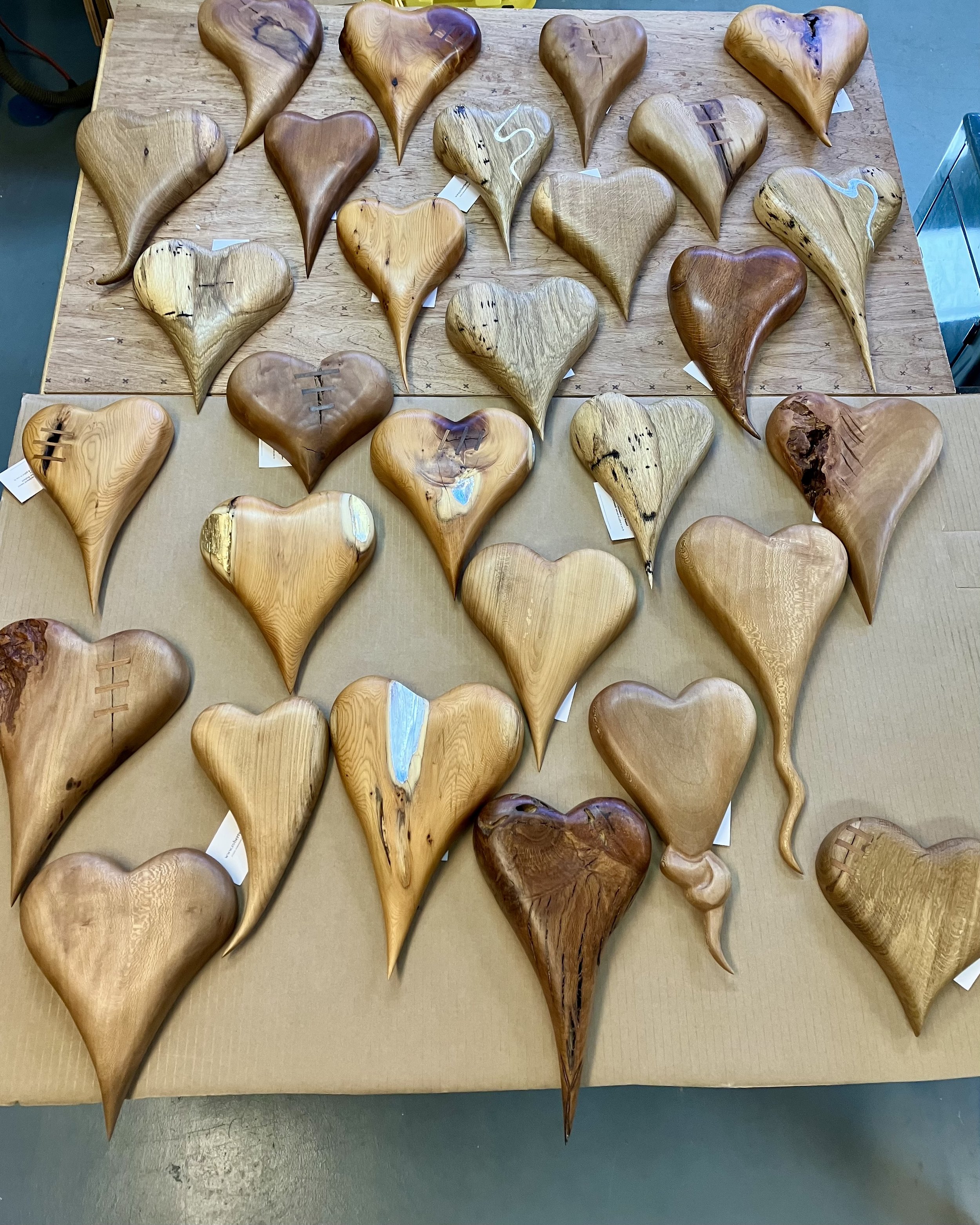 Wooden heart-shaped sculptures arranged on a table, each with unique grain patterns and some with decorative stitching.