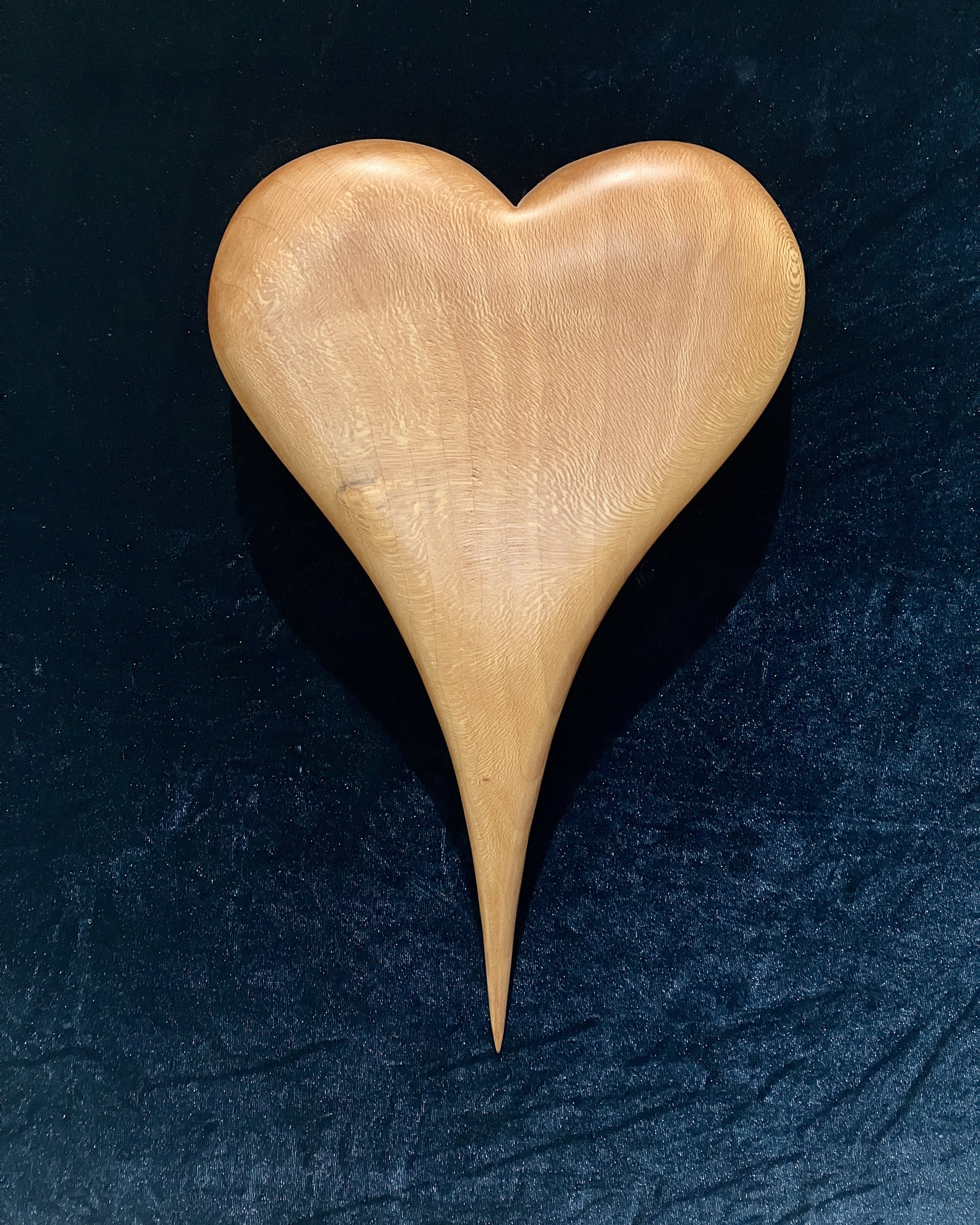 A wooden heart-shaped object with a pointed bottom, placed on a dark textured surface.