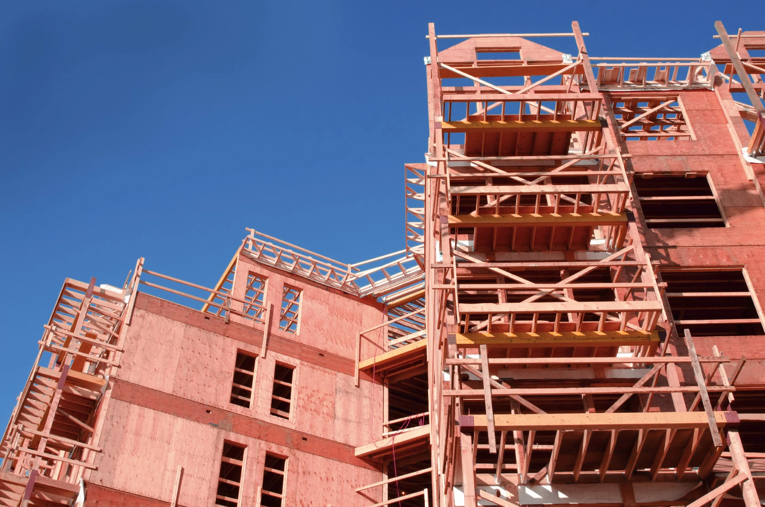 A multi-story building under construction with exposed wooden framing against a clear blue sky.