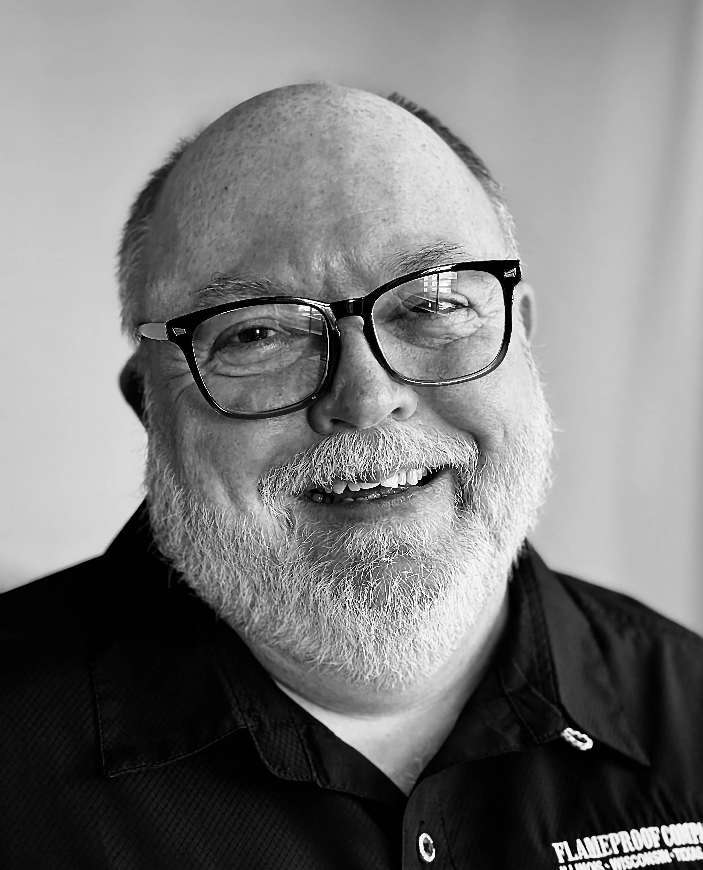 A young man sitting on a cushioned bench against a beige wall, wearing a gray polo shirt and cream-colored pants, with shadows cast on the wall.