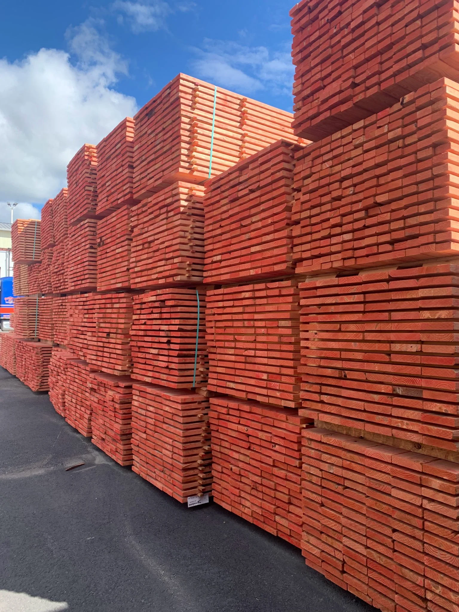 Stacks of red bricks piled on an outdoor pavement, with a blue sky and some clouds overhead.