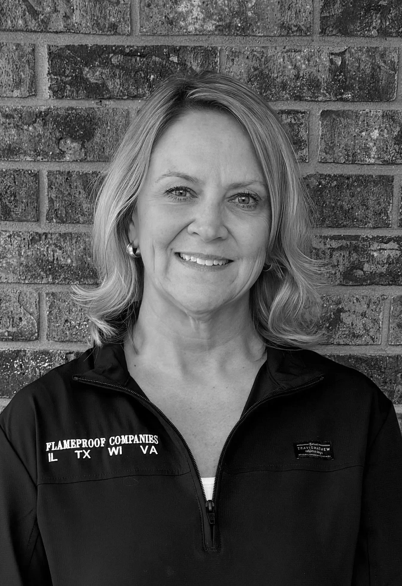 A young Black man in a gray polo shirt and beige pants sitting on a white couch in a room with neutral-colored walls.