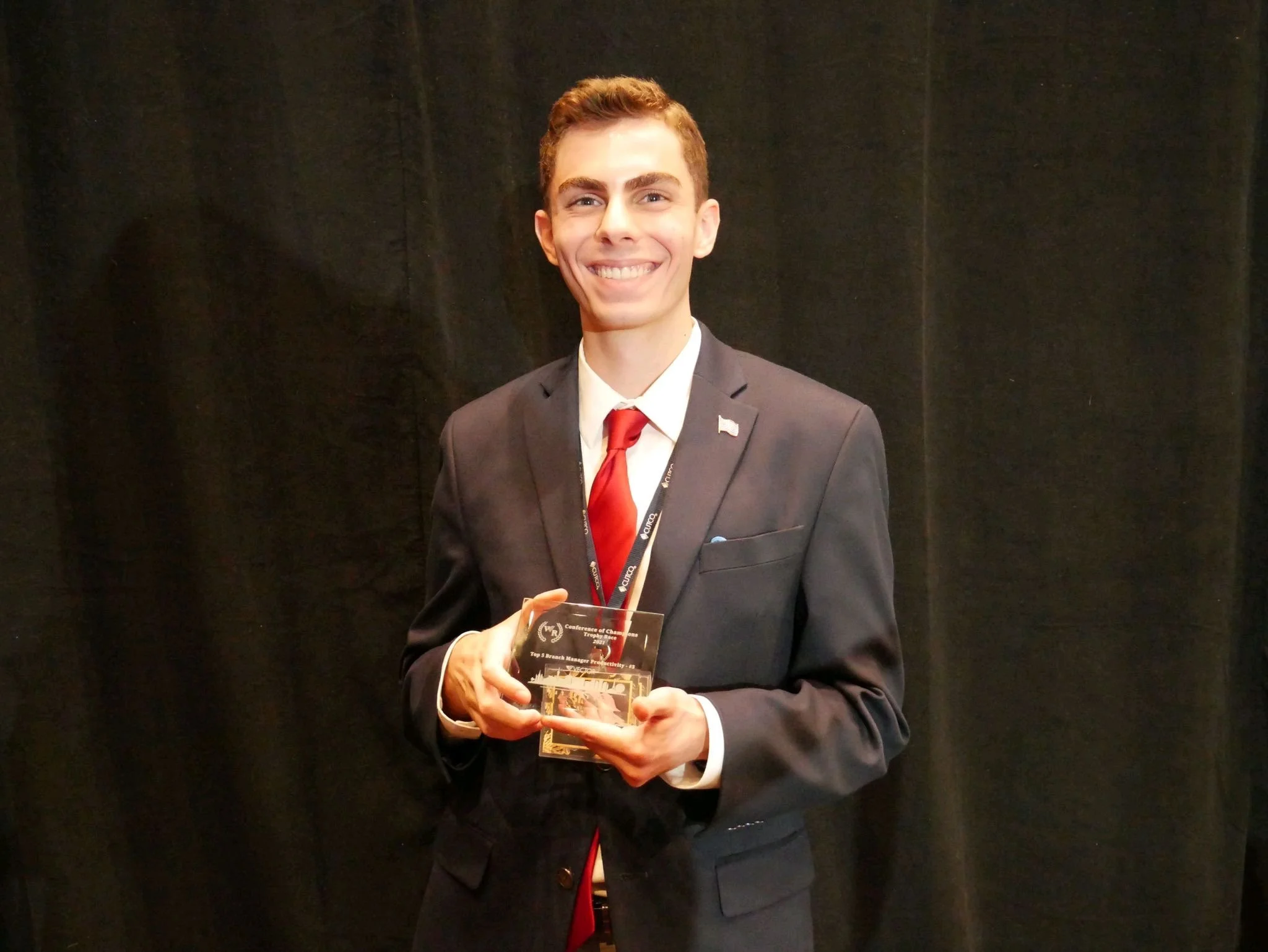 smiling young man with brown hair and a suit holding a trophy