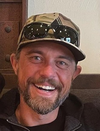 close up on smiling man with a beard wearing hat with sun glasses on top