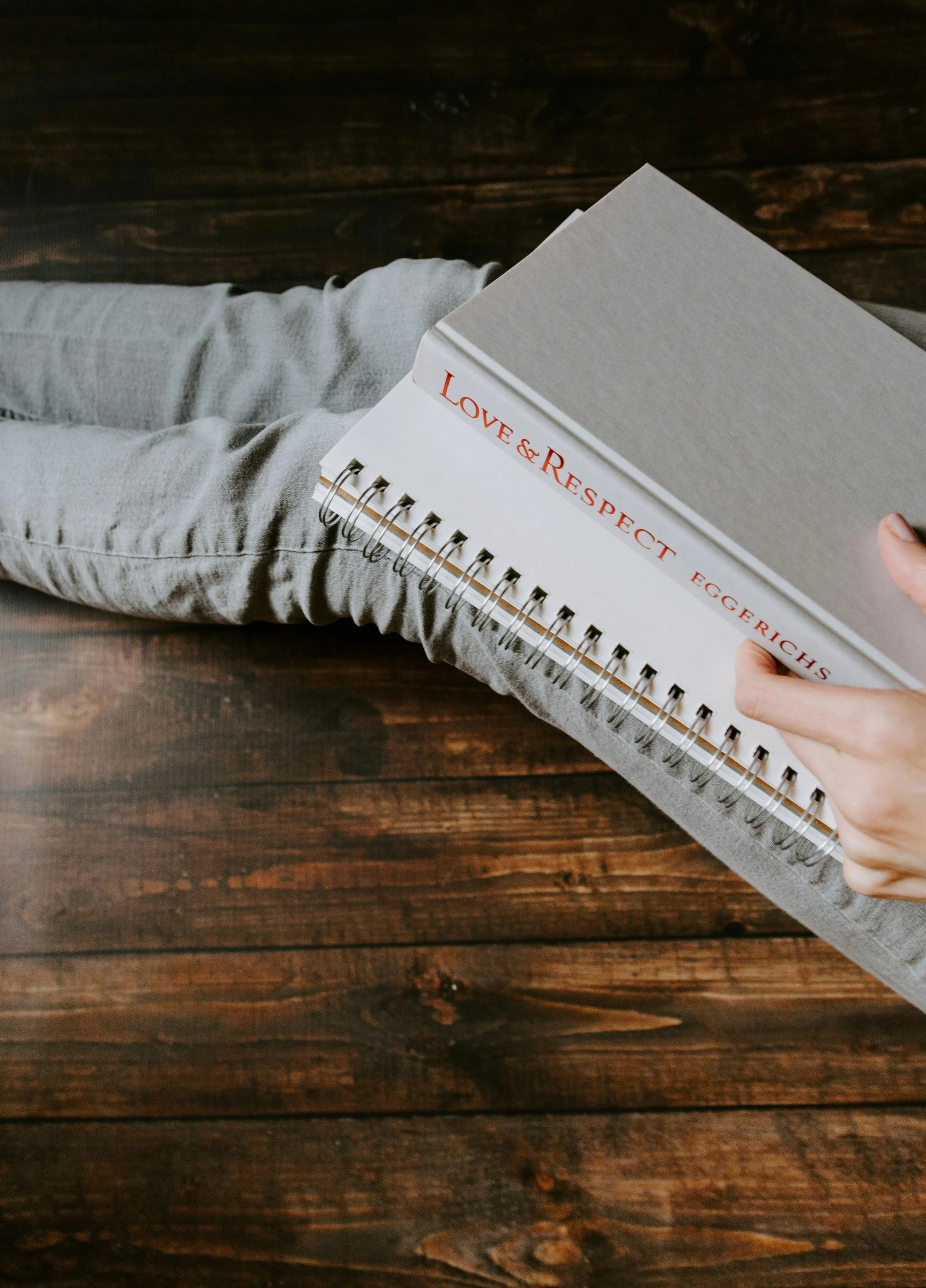 Dallas mental health counselor sitting on a wooden floor reading a spiral-bound notebook titled 'LOVE & RESPECT' with the author's name, Eggers.