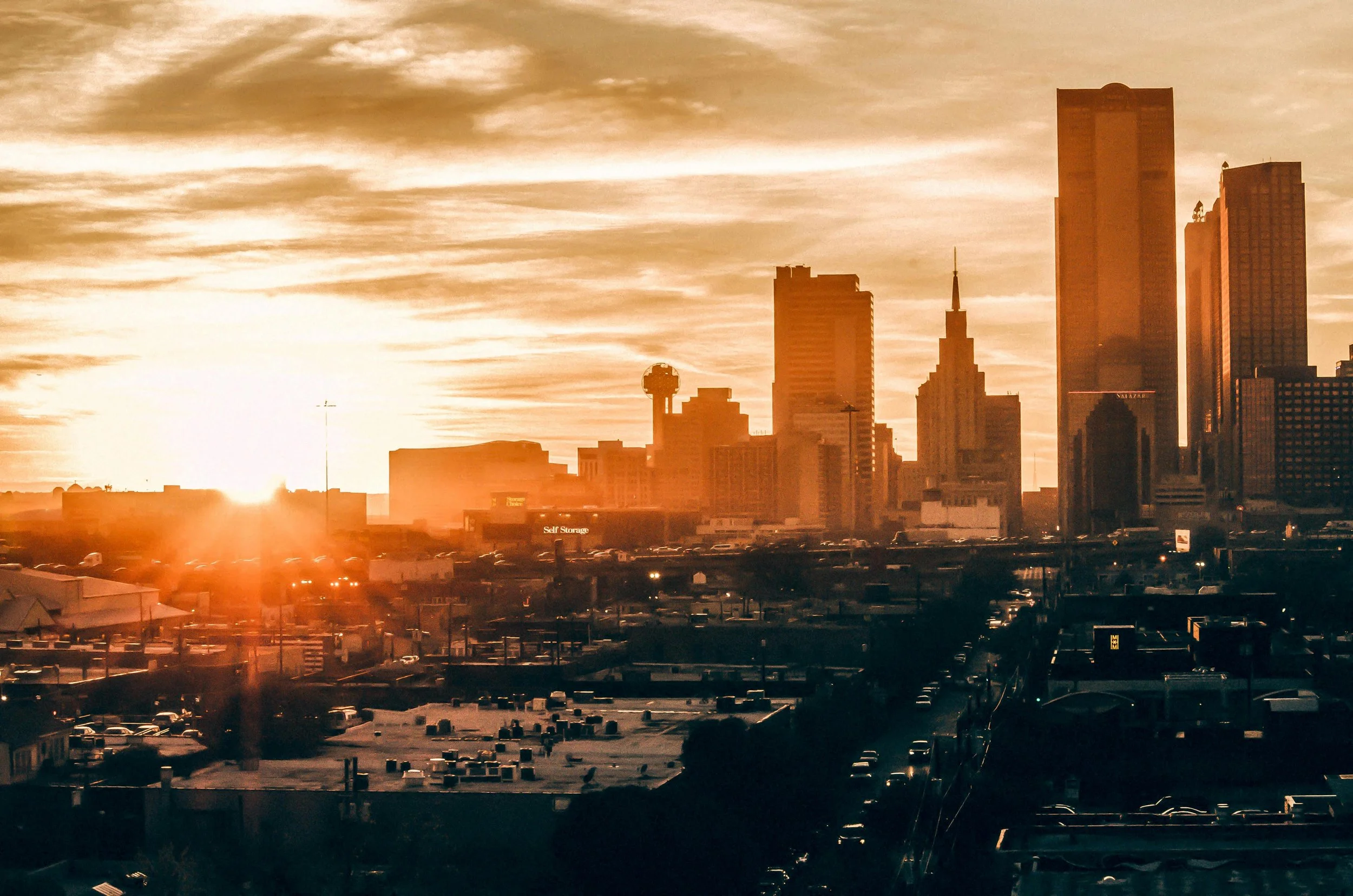 Sunset over a North Dallas skyline with tall skyscrapers and a vibrant orange sky.