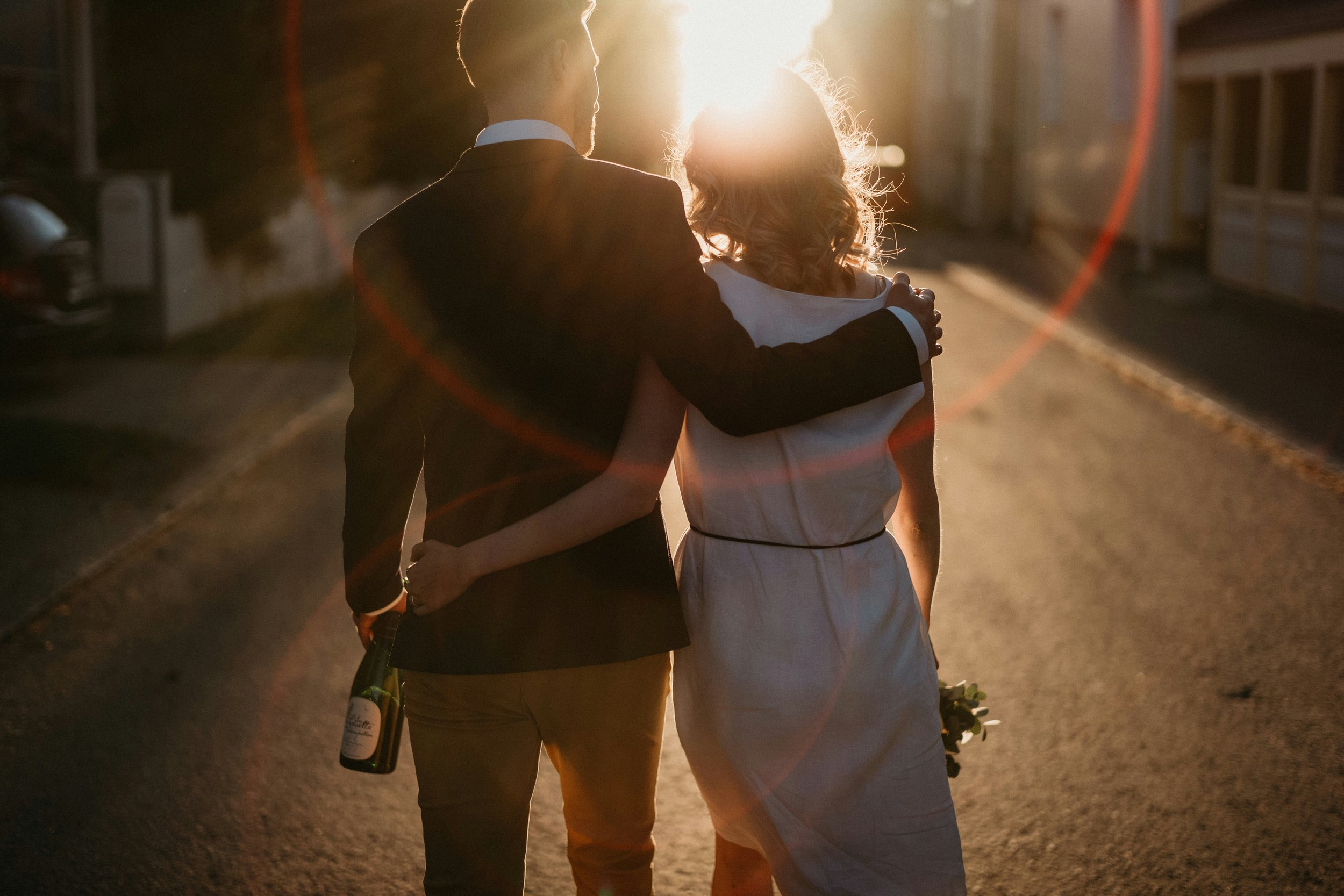 A Dallas premarital couple walking down a street during sunset, with the man holding a wine bottle and the woman holding flowers.