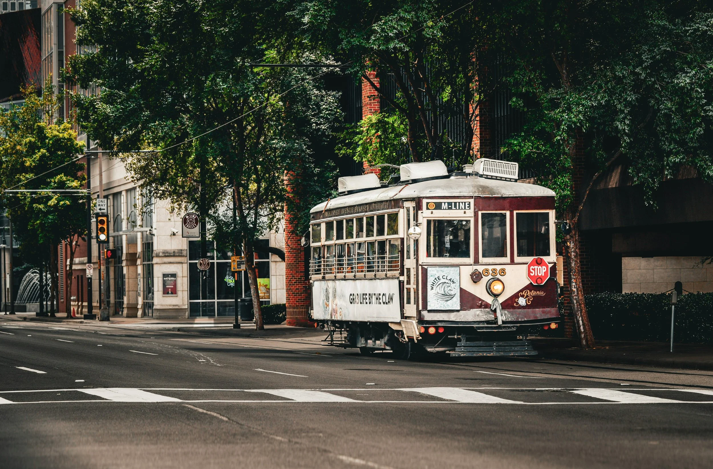 Vintage McKinney Ave streetcar traveling on an Uptown Dallas city street with buildings and trees in the background.