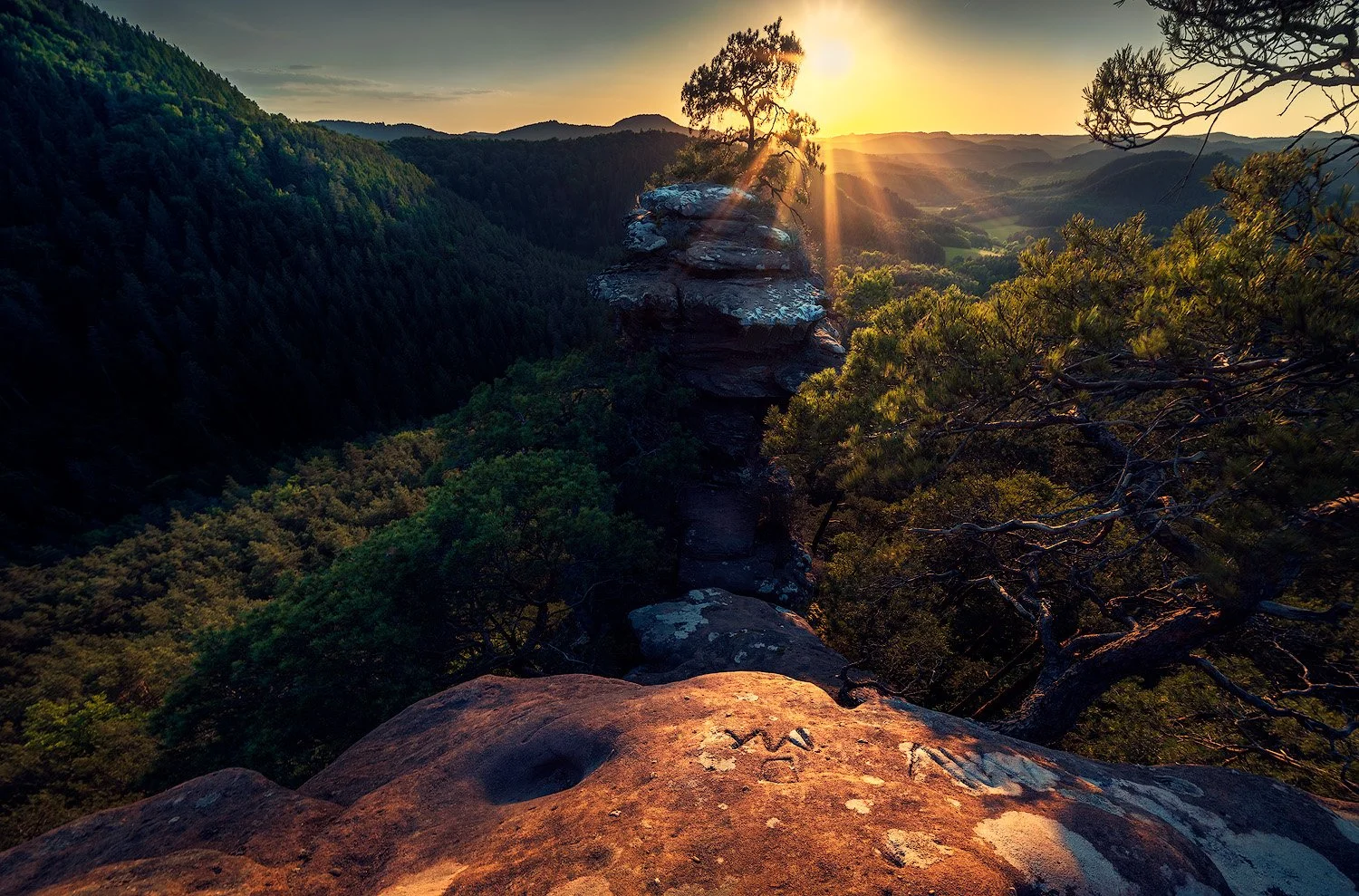Sonnenuntergang über einem valley mit einer Felsformation und einem einzelnen Baum.