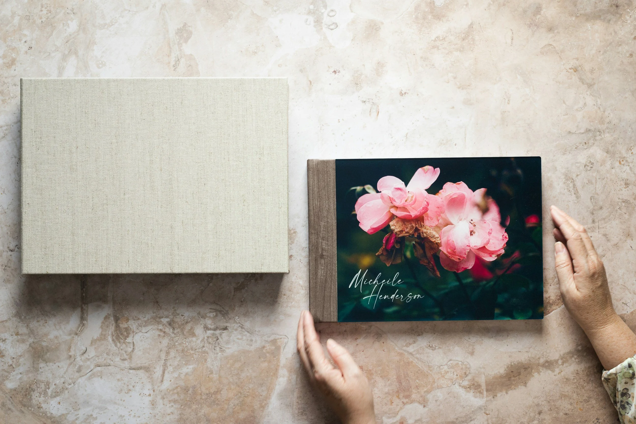 Ein geöffnetes Fotoalbum mit einem blumigen Titelbild und einer Hand, die es hält, auf einer Marmoroberfläche.