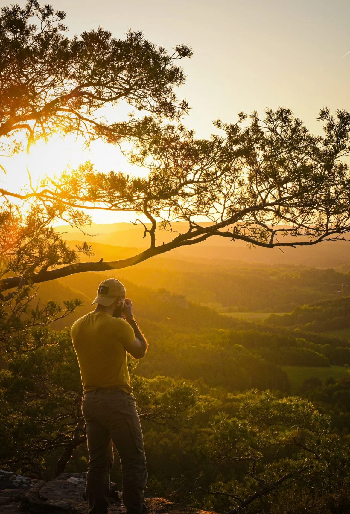 Ein Mann fotografiert während des Sonnenuntergangs die Landschaft, umgeben von Bäumen.