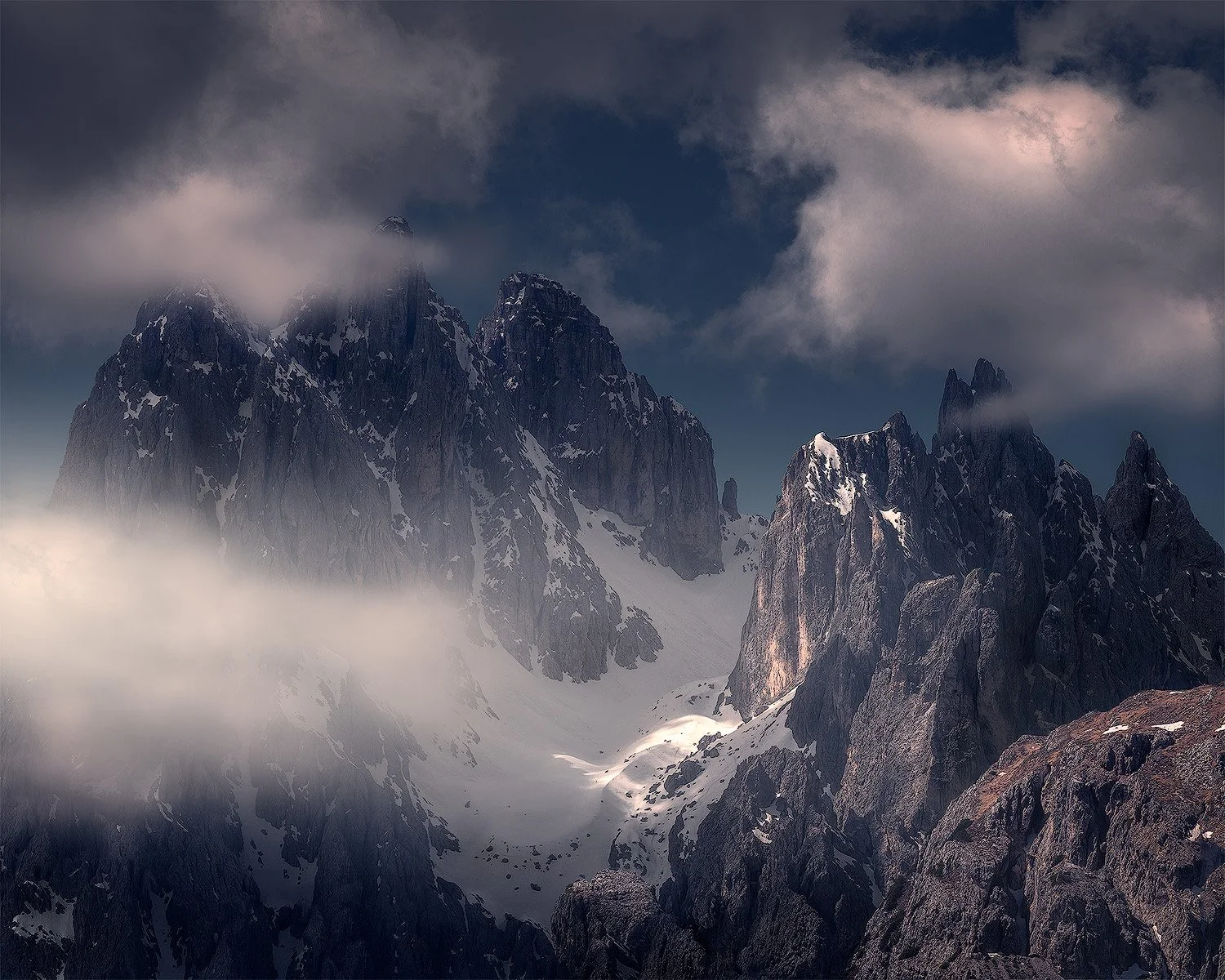 Berglandschaft mit hohen, schneebedeckten Gipfeln und Wolken am Himmel.