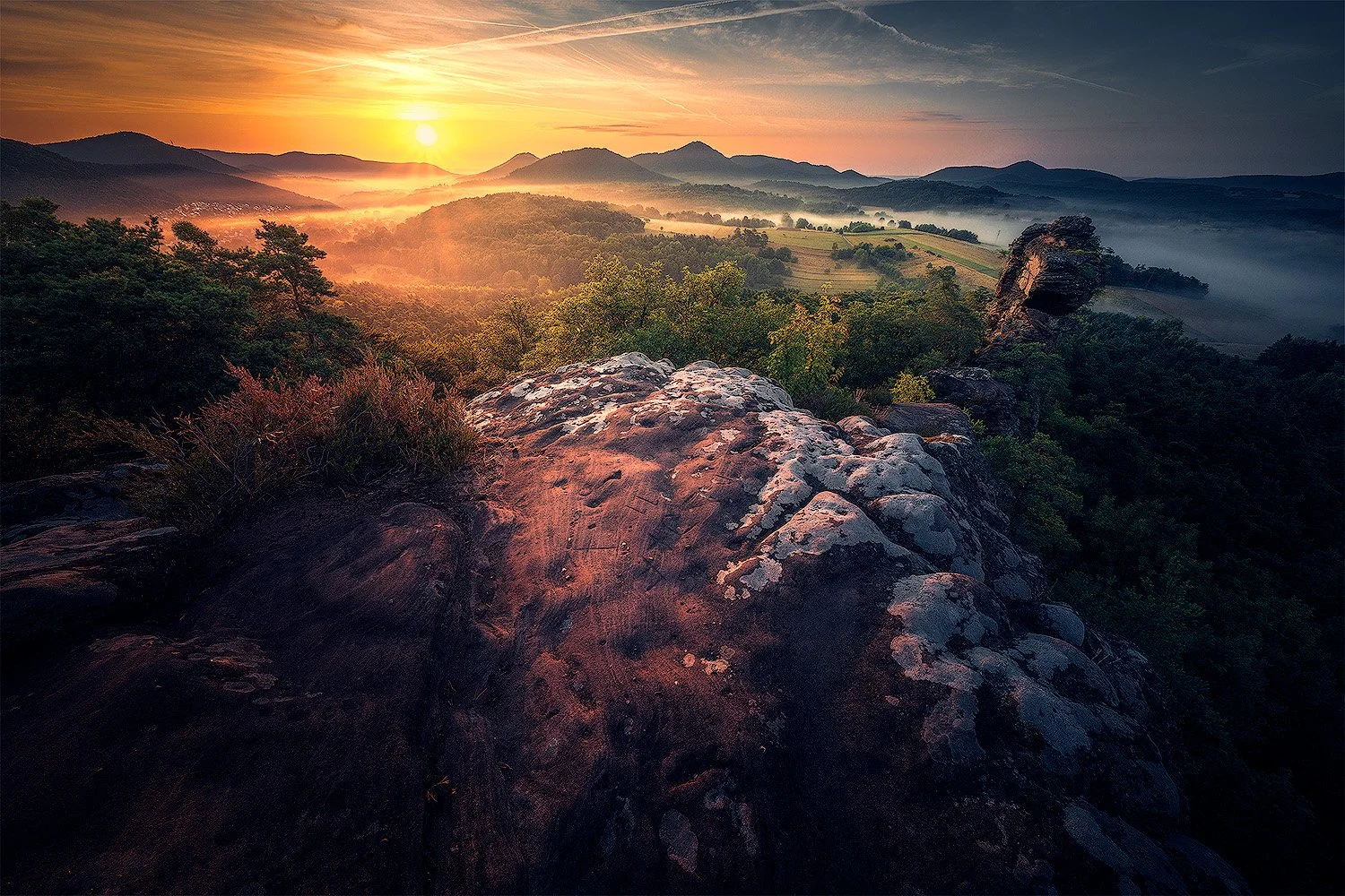 Sonnenaufgang über Bergland, mit Felsen im Vordergrund und Nebel im Tal. Pfälzer Wald.
