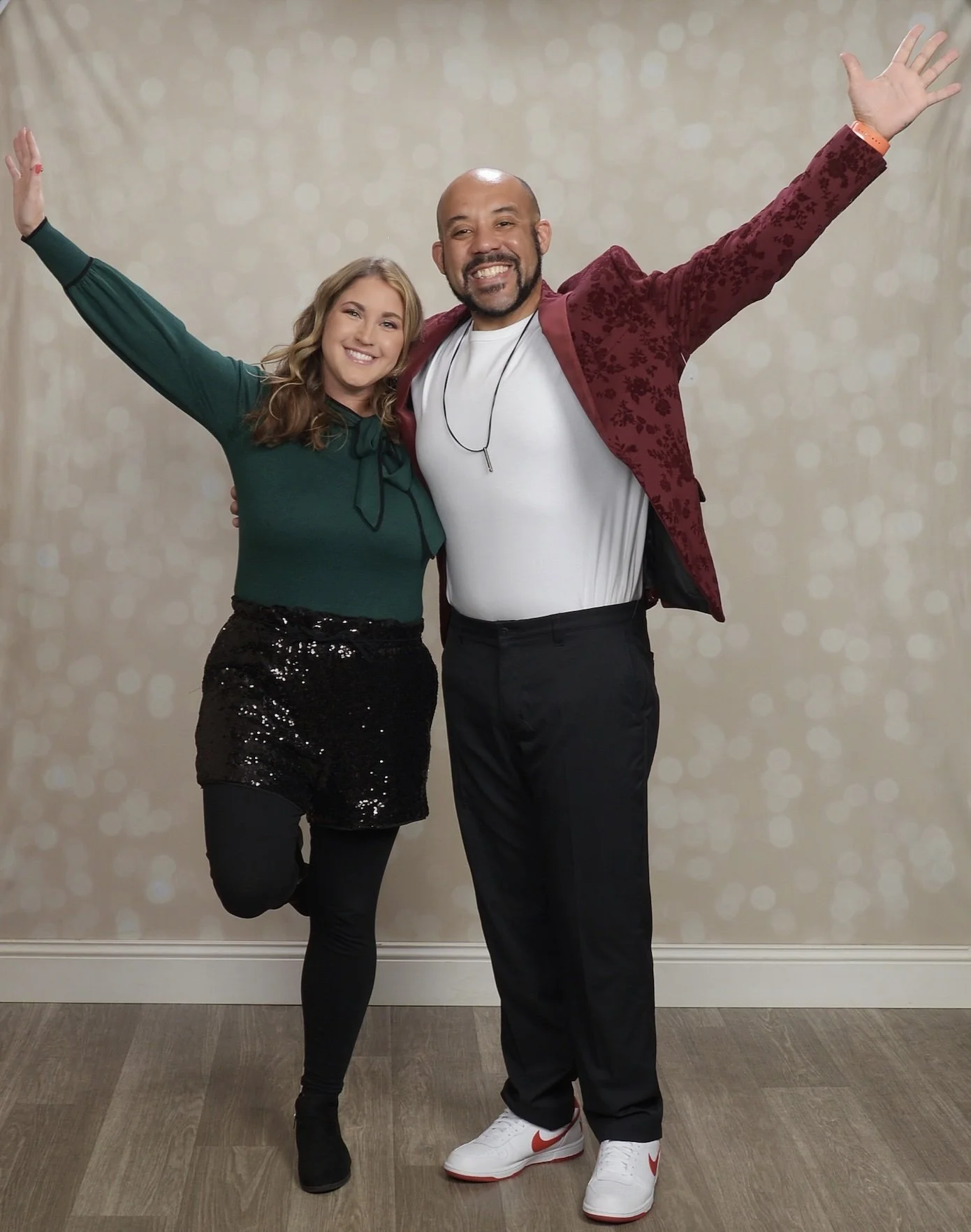 Elizabeth smiling and raising her arms in celebration, standing on a wooden floor against a beige, bokeh background.