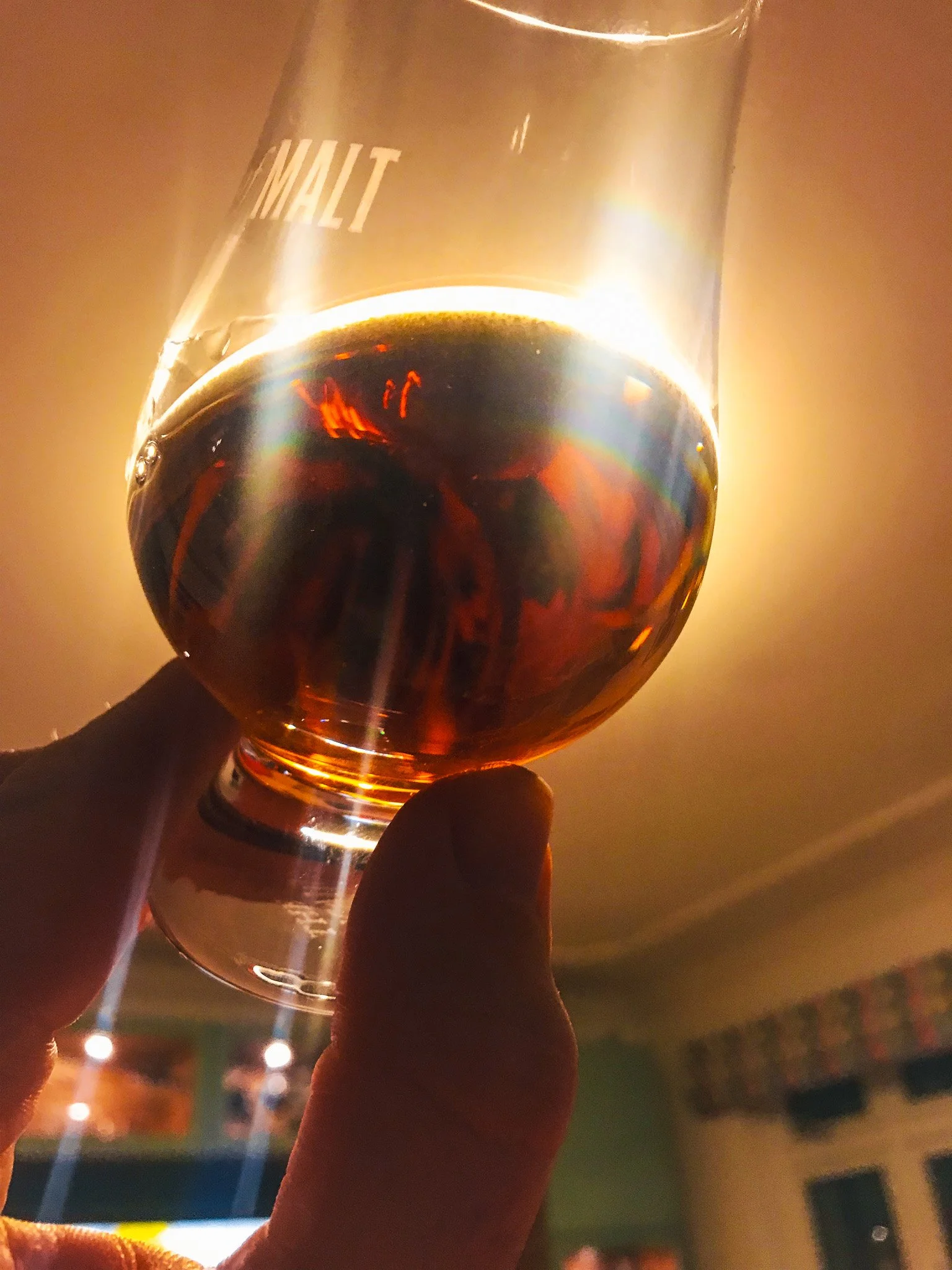 A hand holding a glass of dark amber liquid against a bright light source.