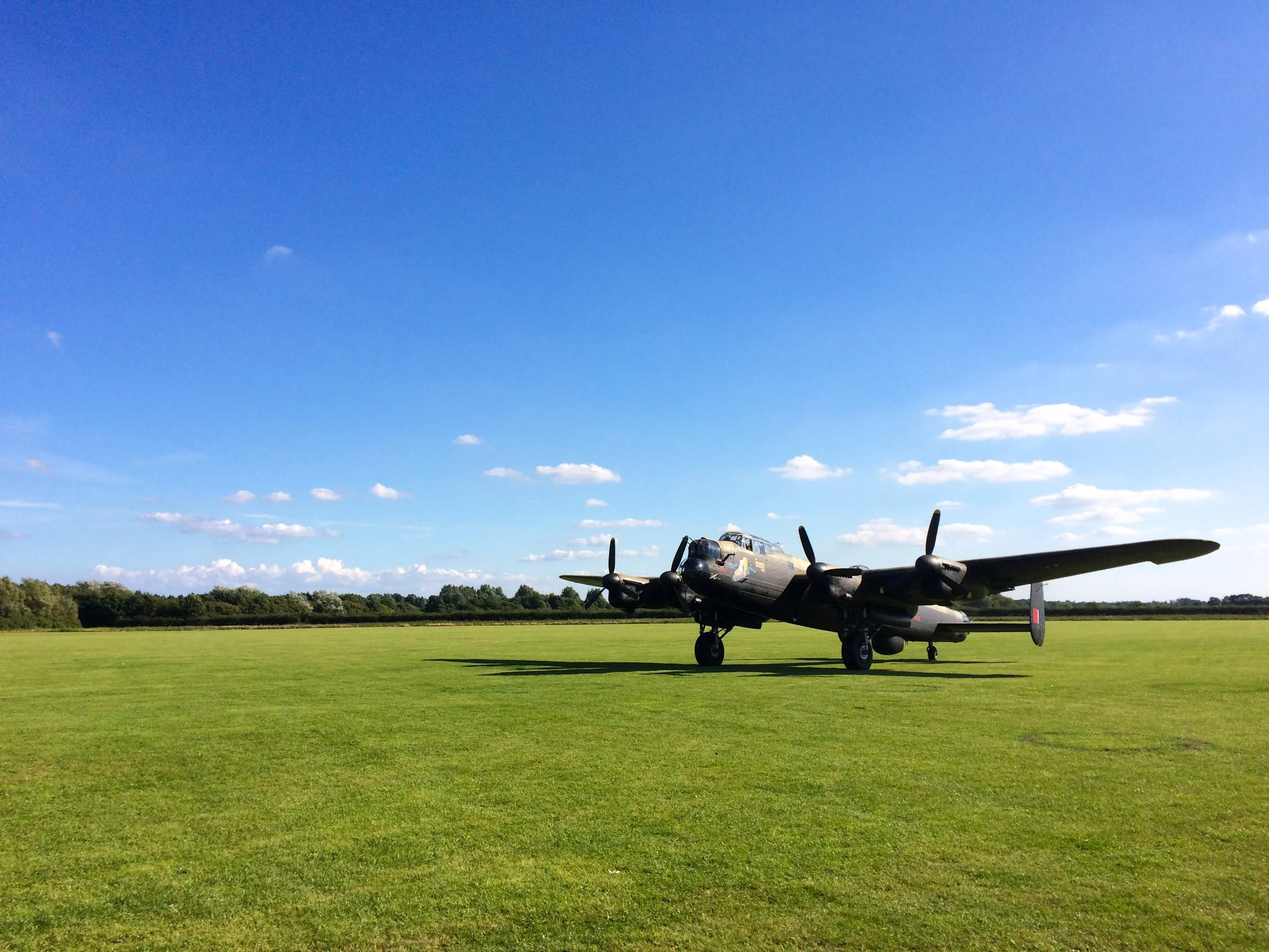 A vintage military aircraft parked on a grassy airfield with a clear blue sky and a few clouds above.