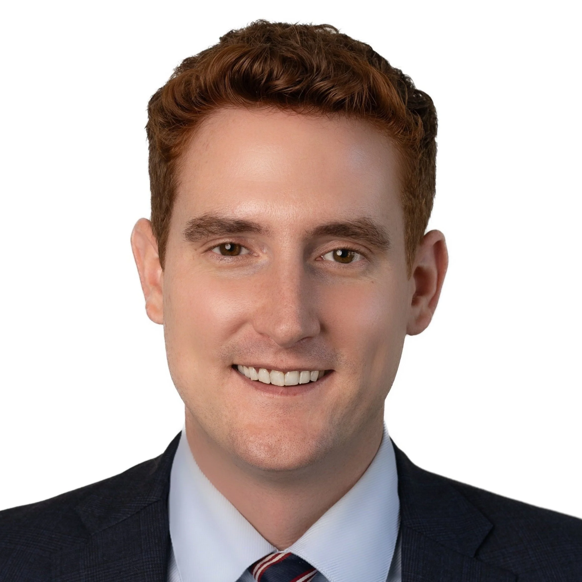 Headshot of a young man with red hair, wearing a dark suit, white shirt, and striped tie, smiling against a white background.