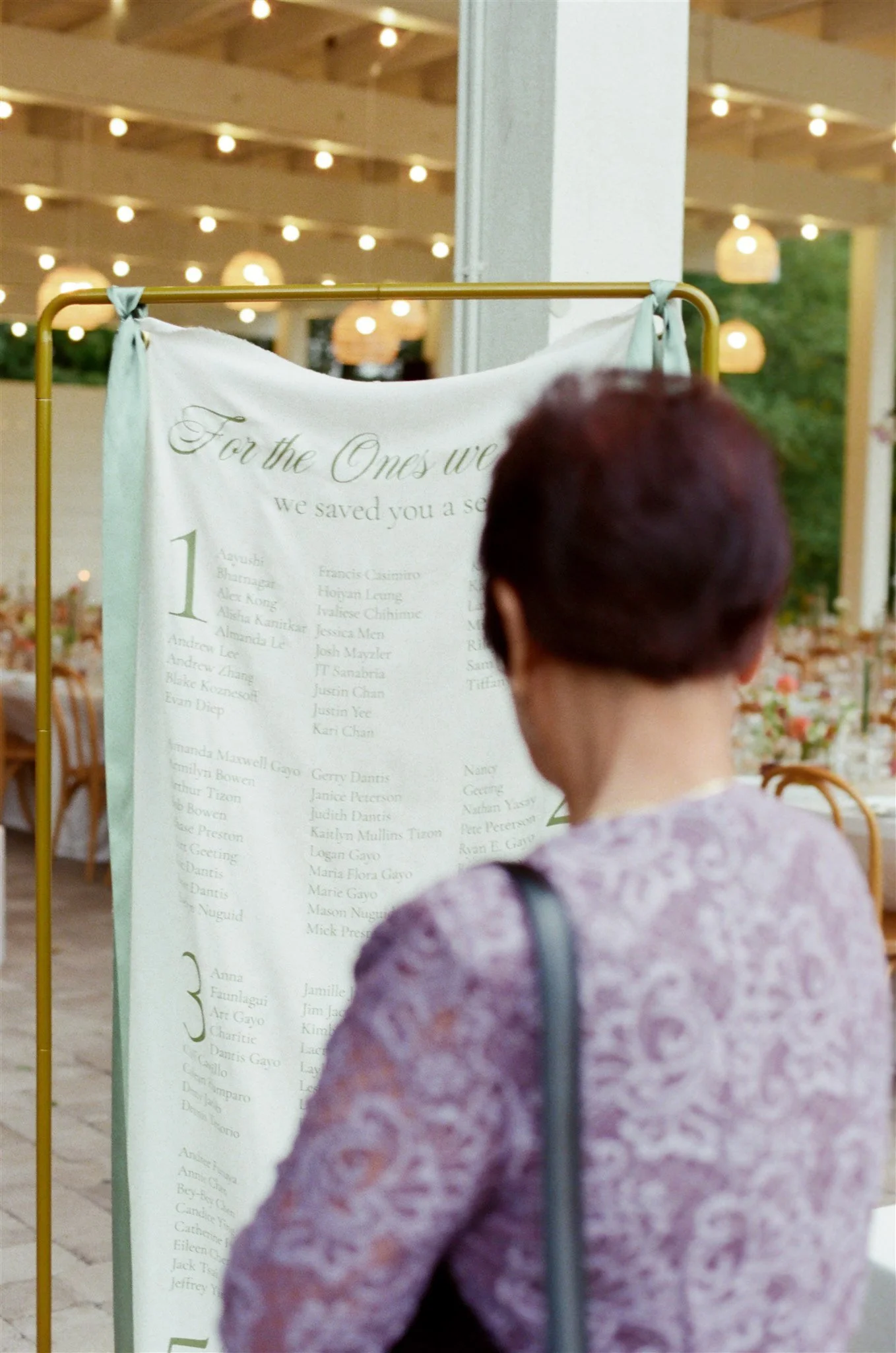 A woman with short reddish hair reading a large printed list at an indoor event with warm lighting and wooden ceiling beams.