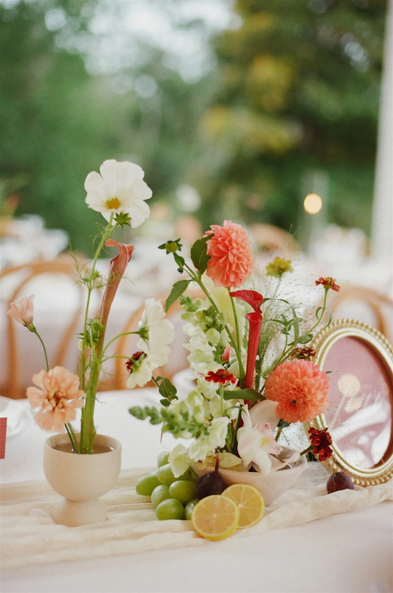 A floral arrangement with white, pink, and red flowers in a white vase, placed on a table with sliced lemons and fresh grapes.
