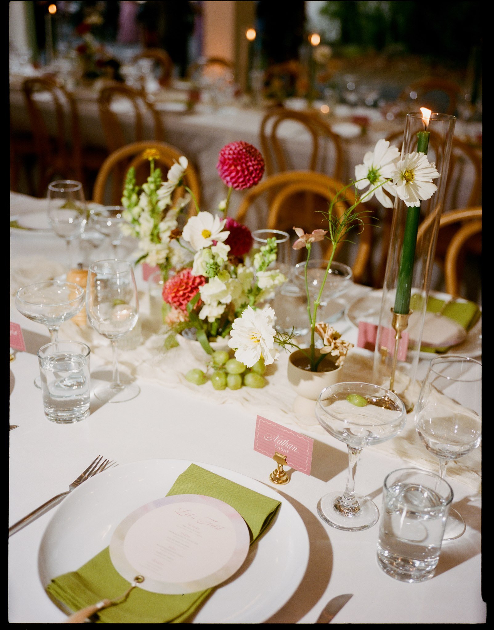 A formal dining table set for a celebration with floral centerpieces, glassware, and menu cards, decorated with candles and elegant tableware.