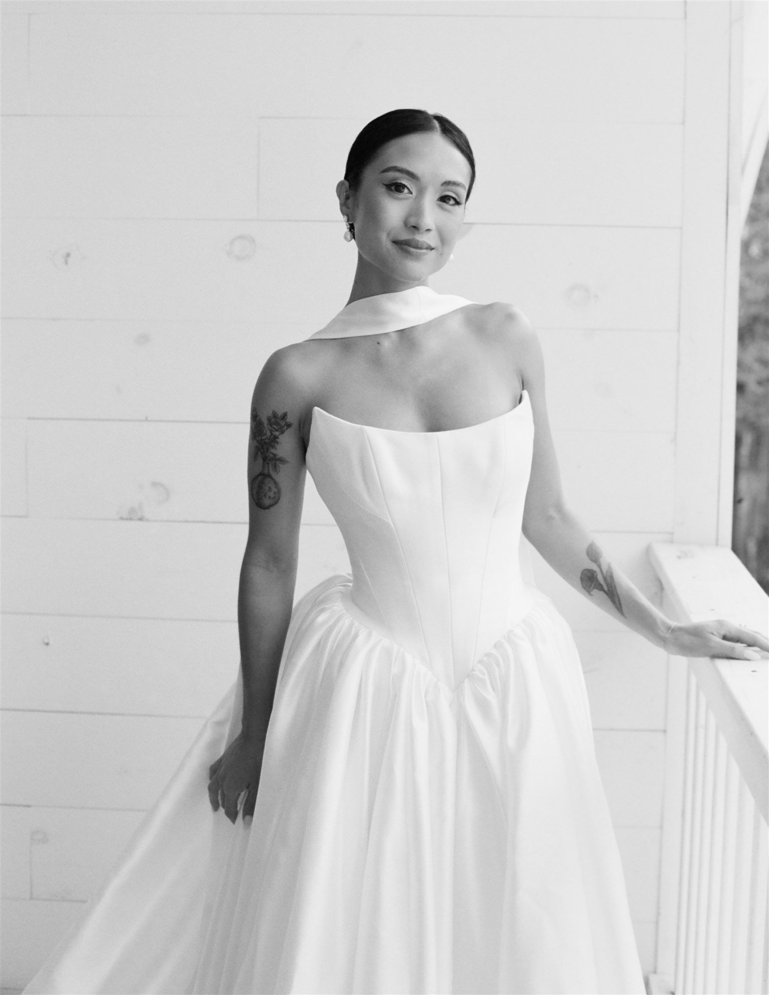 Black and white photo of a woman in a sleeveless dress standing by a window or door with white paneled walls, smiling at the camera.