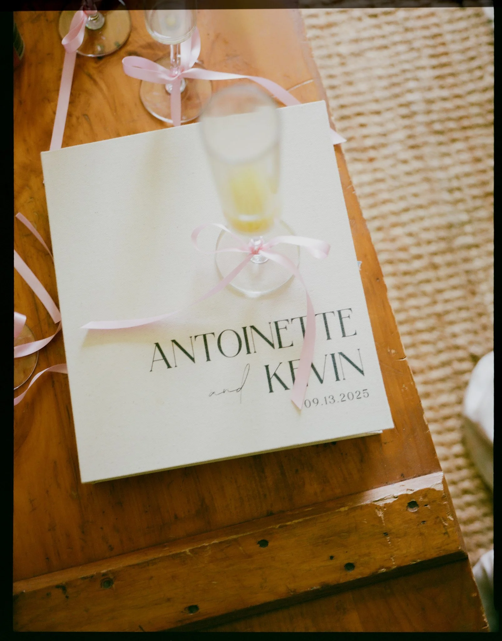 Wedding invitation card with pink ribbons and champagne glasses on a wooden table.