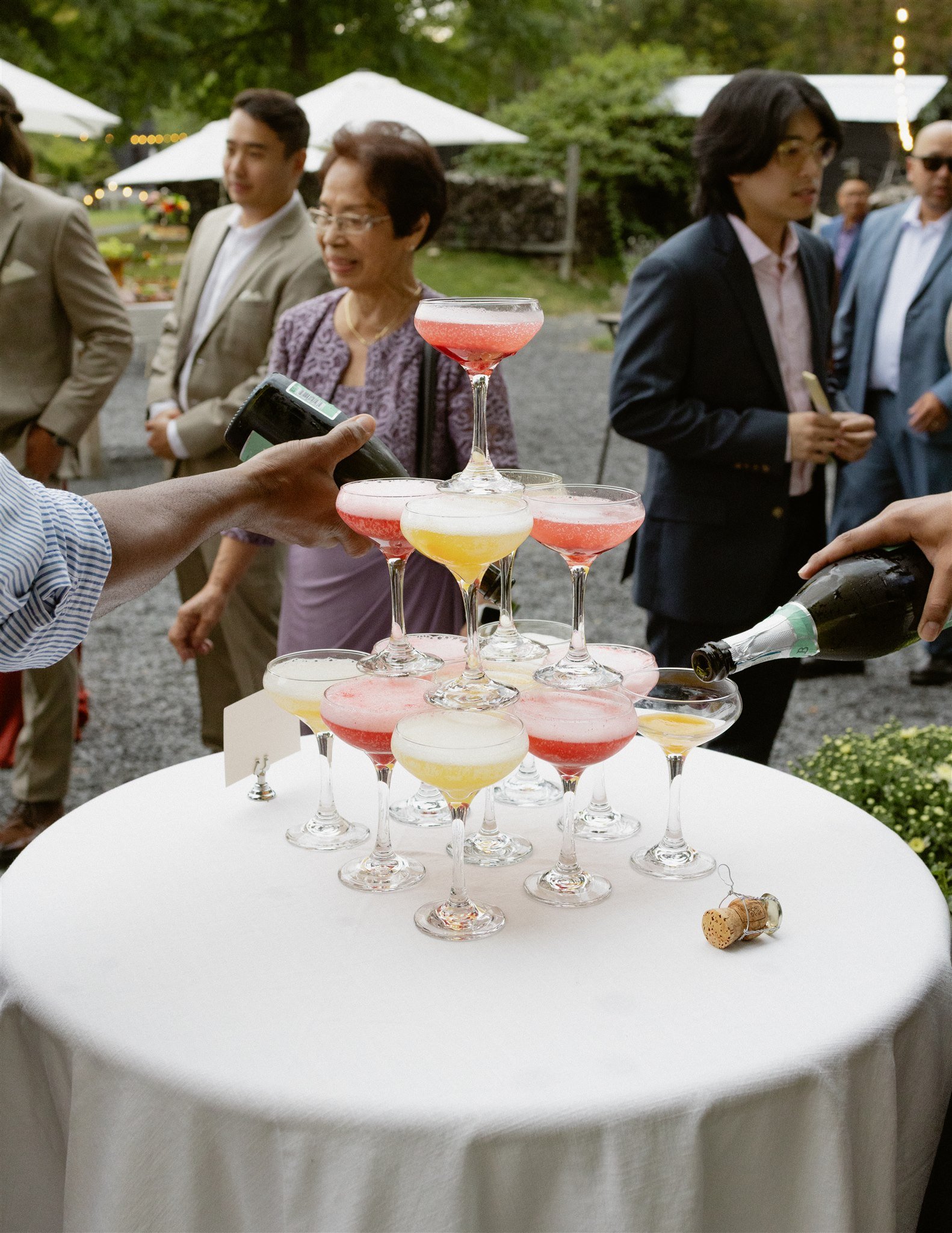 Stacked champagne glasses with pink and yellow beverages on a white table at an outdoor event.