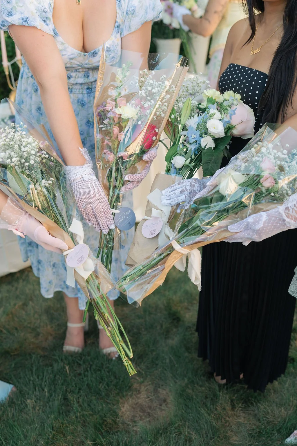 Women exchanging flower bouquets at an outdoor event, with flowers wrapped in clear and brown paper.