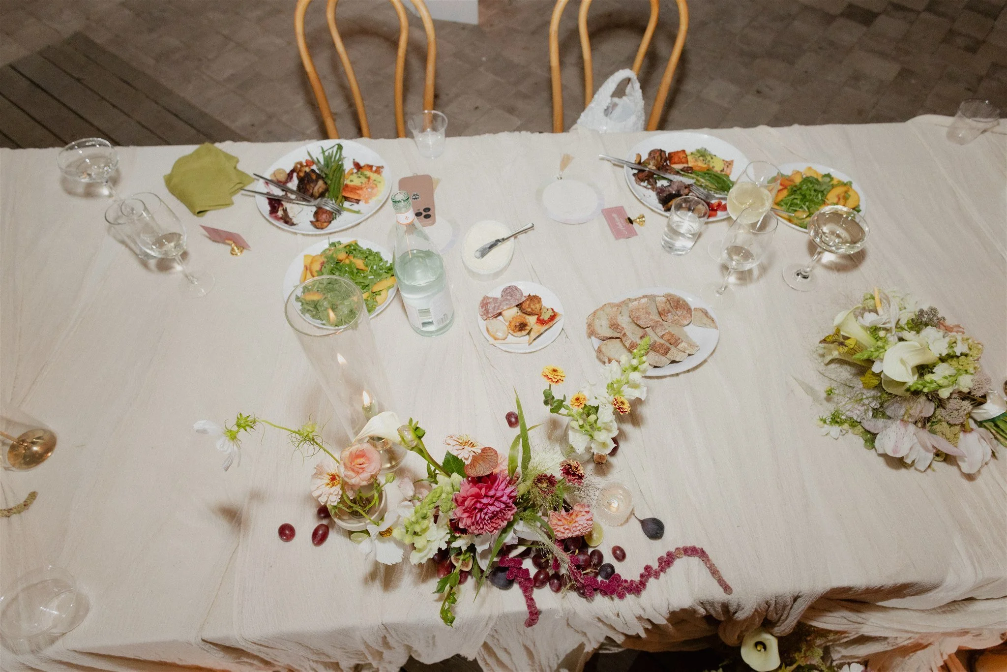A dining table set for a meal with plates of food, glasses of water and wine, and floral centerpieces.