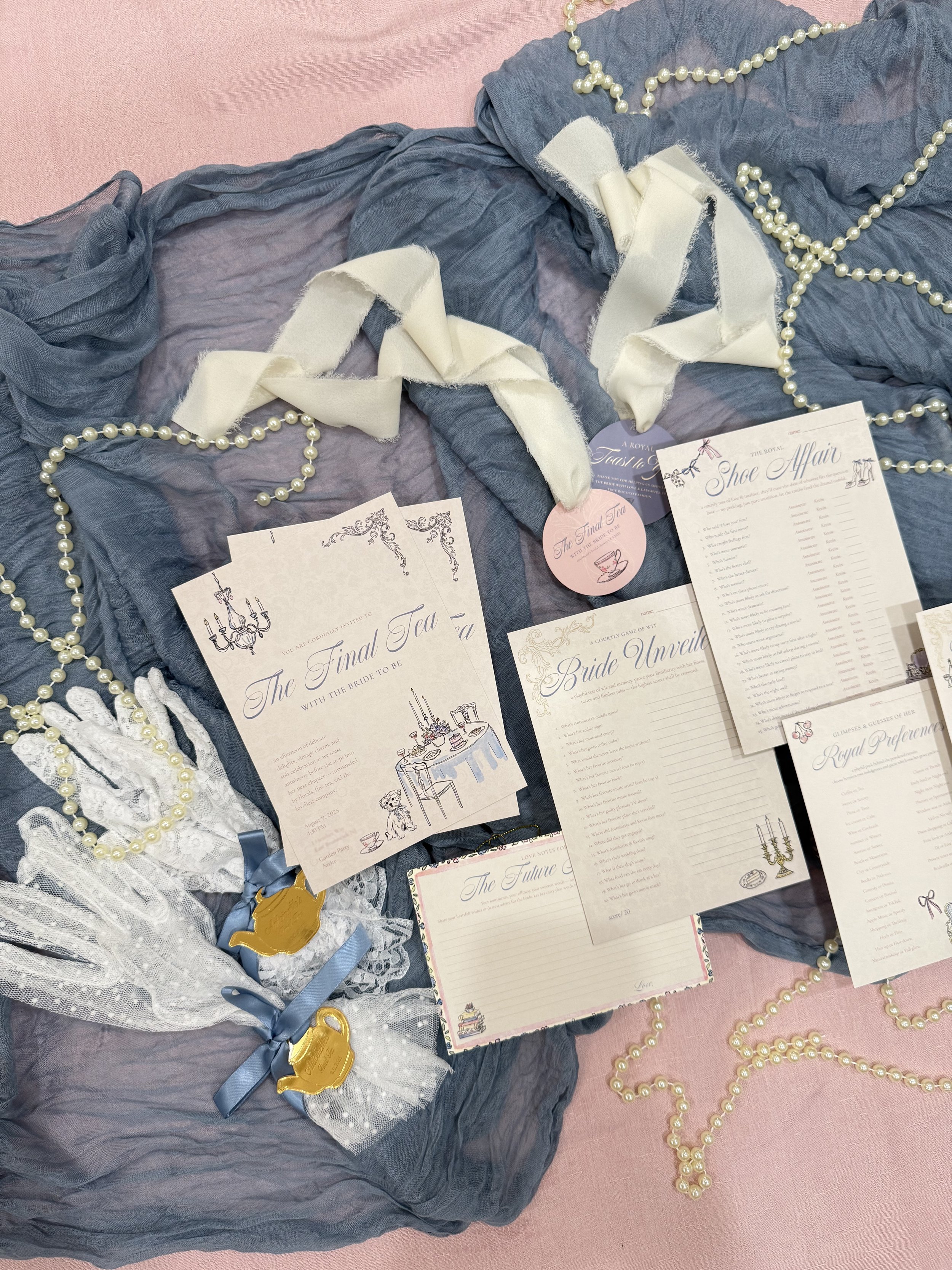 A display of wedding-related items including invitations, pearl necklaces, white lace gloves, and a corsage on a pink and grey fabric background.