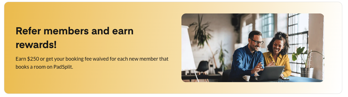 Two people sitting at a table looking at a laptop, smiling, in a bright office with large windows and plants.