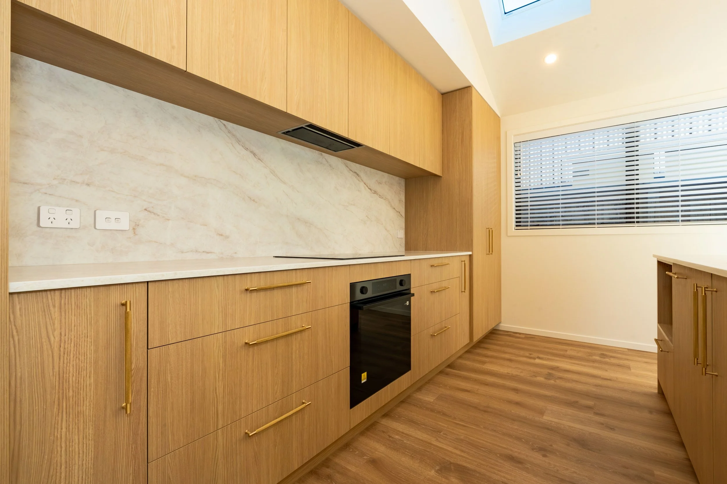 Modern open-plan kitchen with bespoke cabinetry, natural stone benchtops, pendant lighting, and a spacious island, showcasing timeless interior design in Hanley's Farm, Queenstown.
