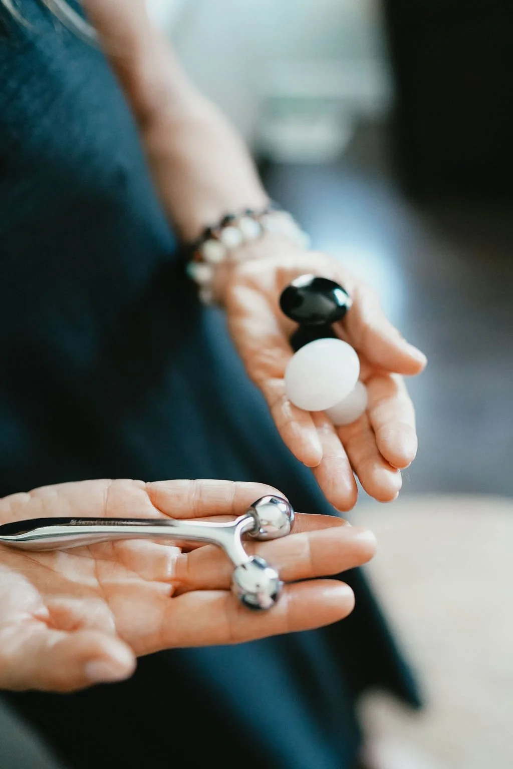 Close-up of a person's hand wearing multiple bracelets, holding a curling wand and three hair styling rollers. Booking a glow state facial in stratford ontario.