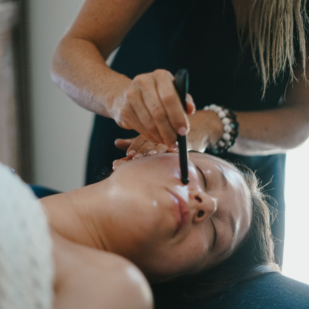 A woman receiving a facial treatment while lying down, with her eyes closed, as a professional applies a tool near her face.