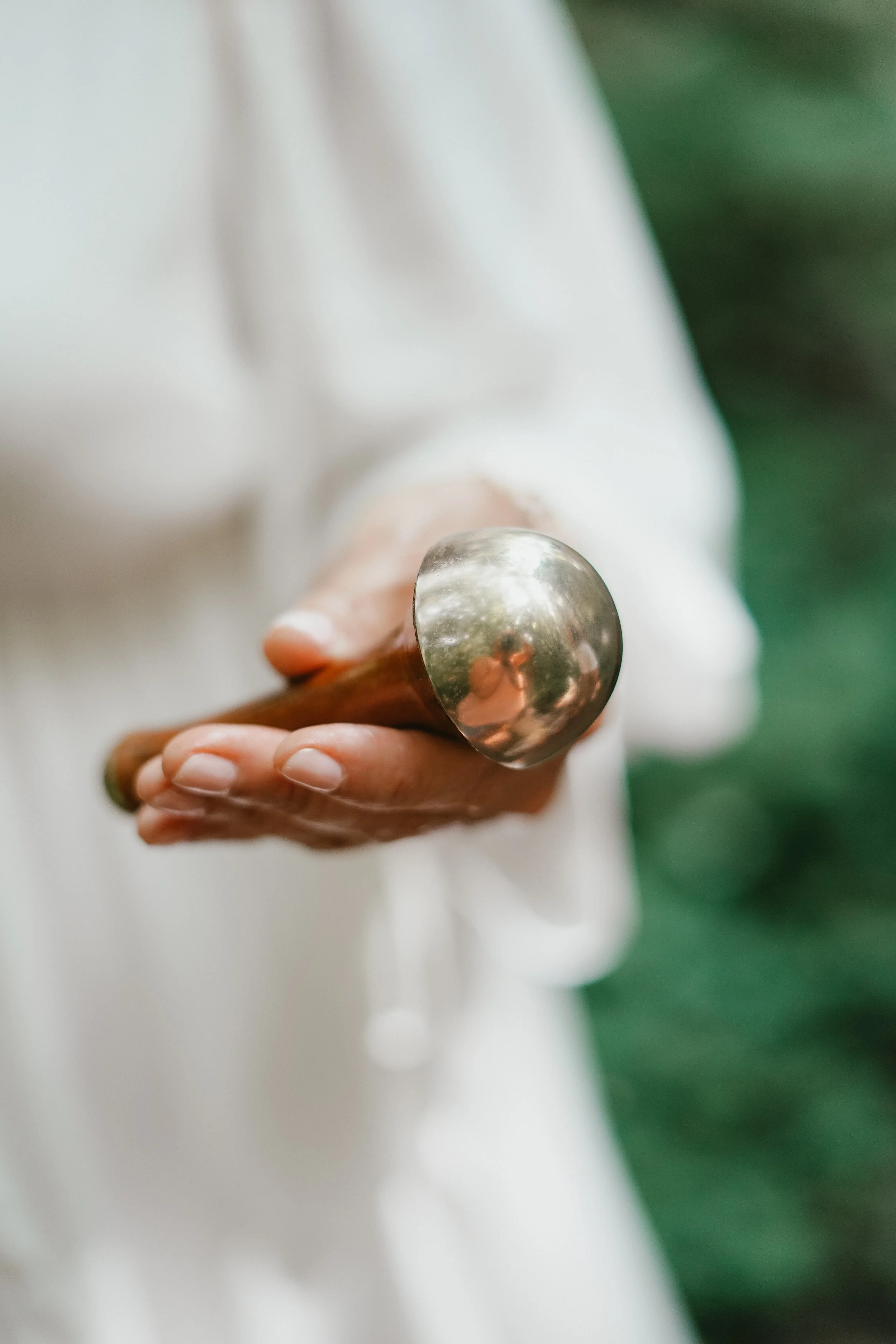 Close-up of a hand holding a metal Buddhist gong mallet, with a blurred background. Booking a glow state facial in stratford ontario.