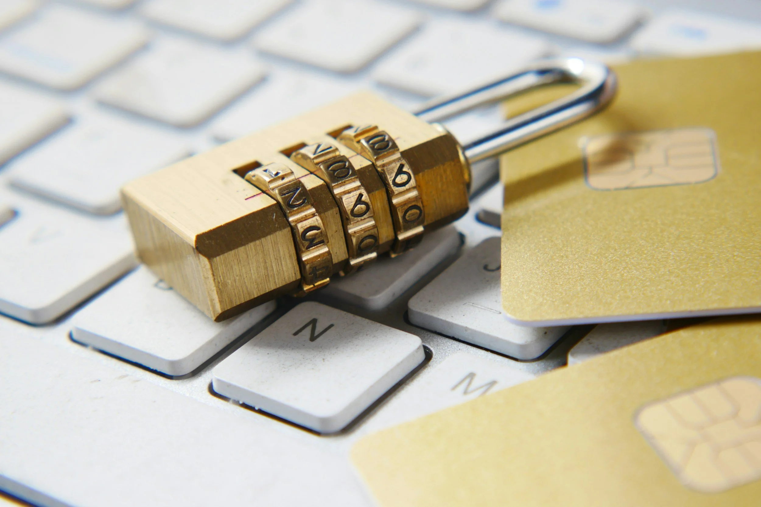 Close-up of a computer keyboard with a yellow lock with four dials and a golden credit card on top of the keyboard.