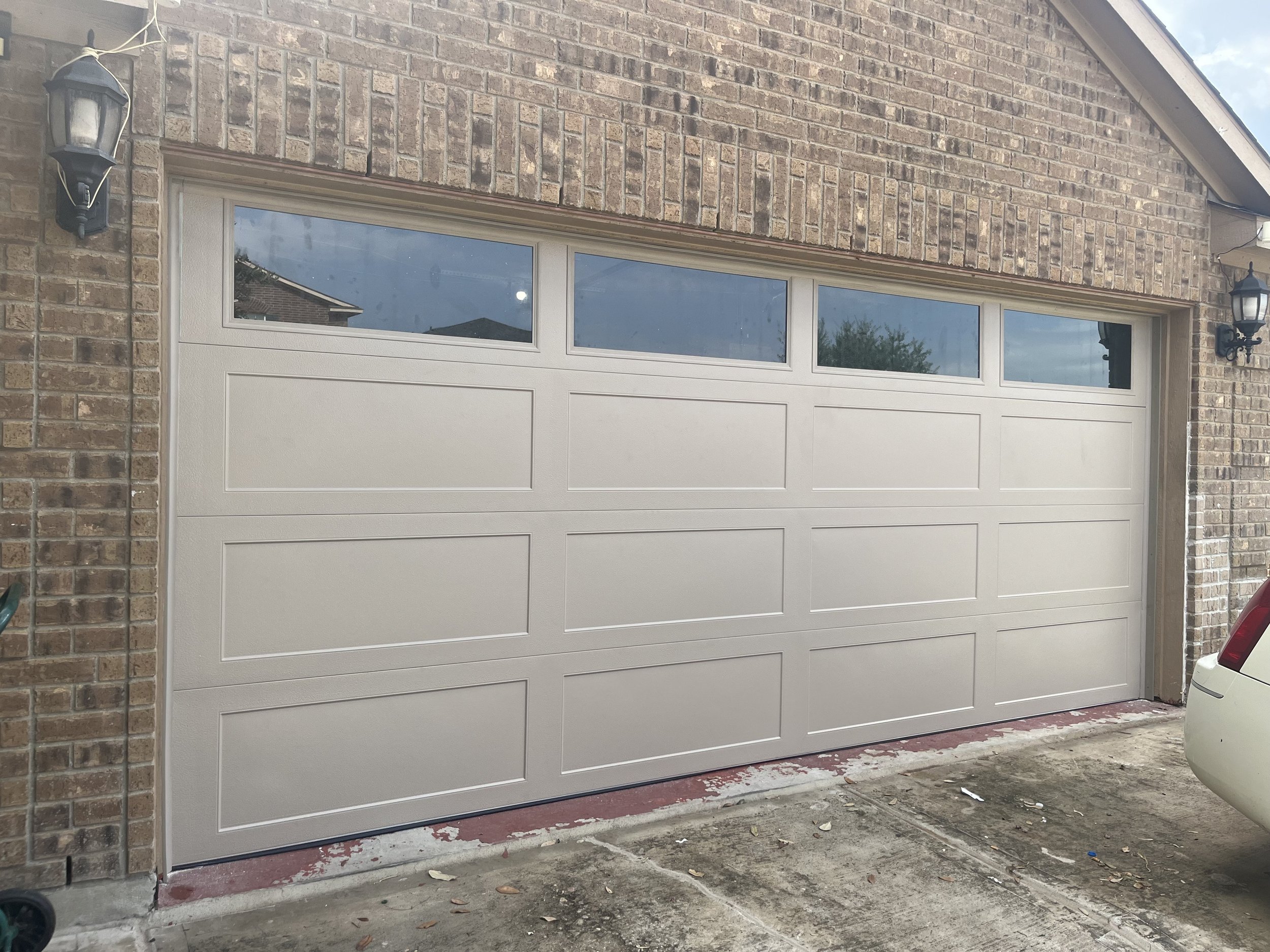 A close up view of a desert tan garage door with windows across the top and recessed panels on the rest of the door.