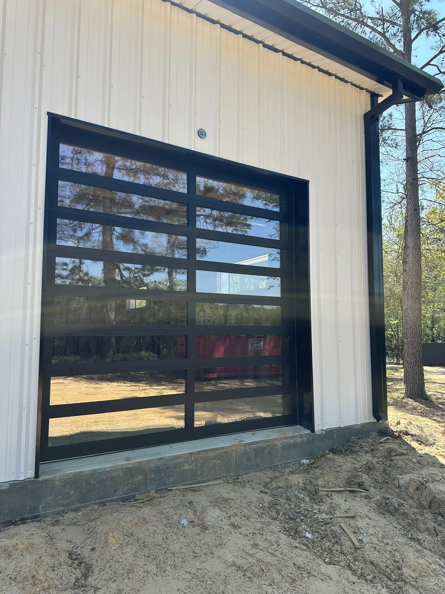 An exterior view of a modern black 12x12 fullview overhead door that mirrors the surrounding outside space with it's tinted glass.