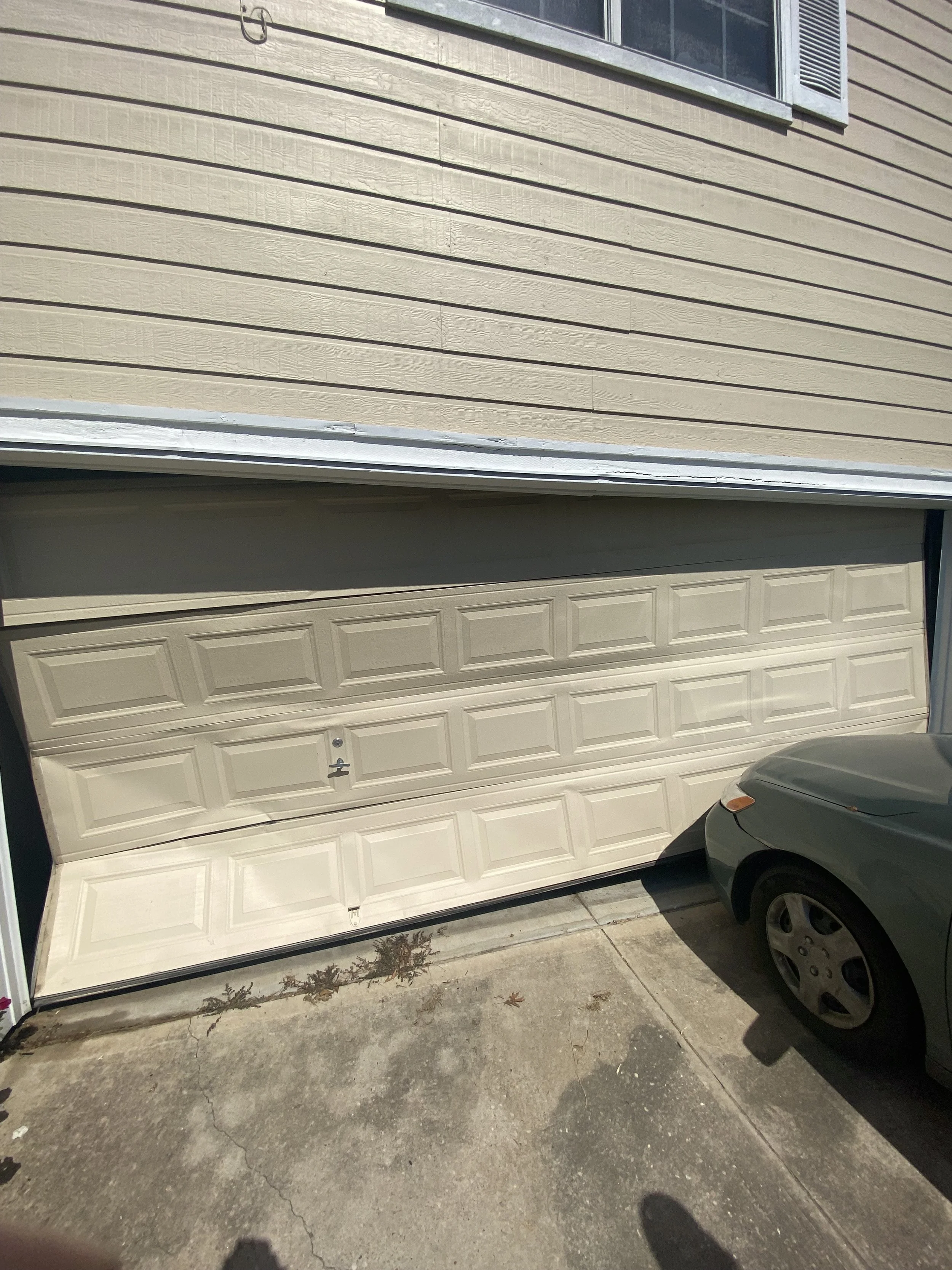 A beige garage door that was hit and crumpled in on itself that needed to be replaced.