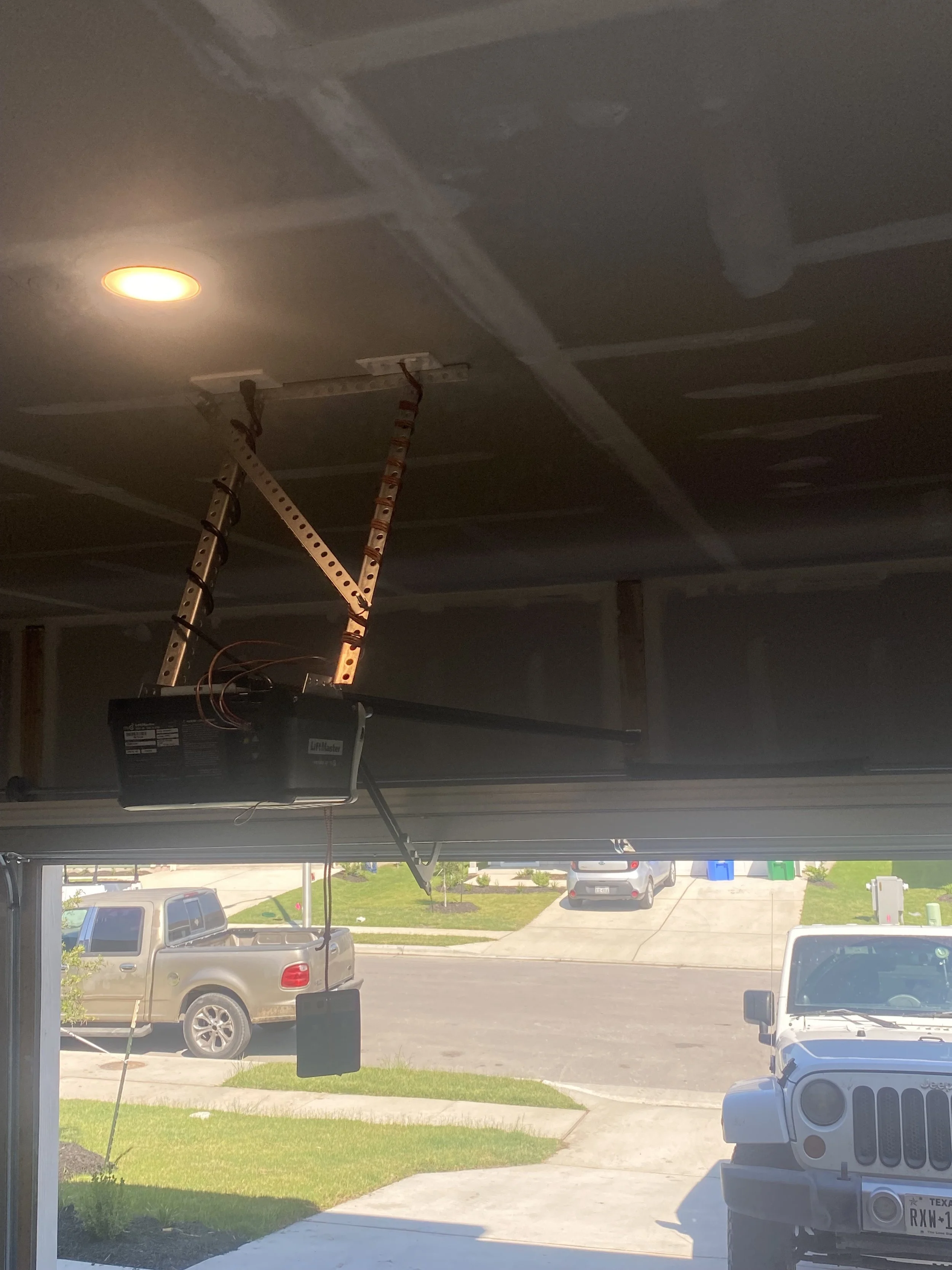 Liftmaster garage door opener installed in a garage with the ceiling partially finished, and a view of parked cars outside