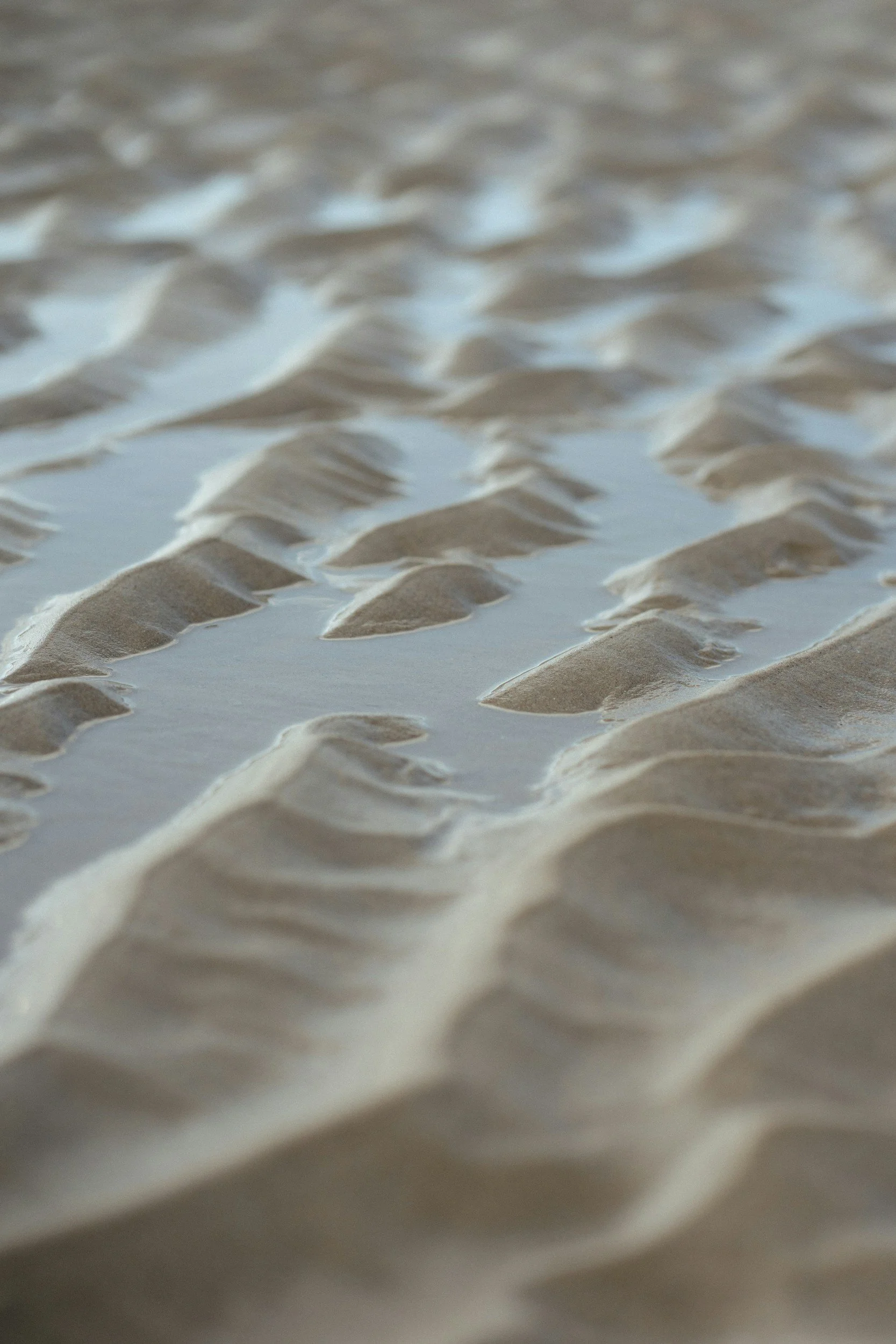 Close-up of sand with ripples and shallow water on a beach.