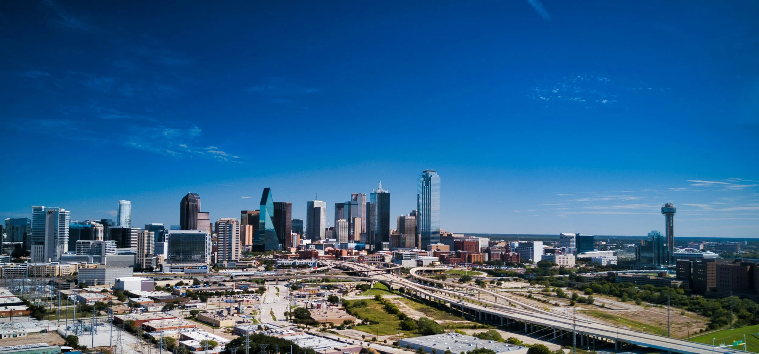 Skyline of Dallas, Texas with tall skyscrapers, highways, and a clear blue sky.