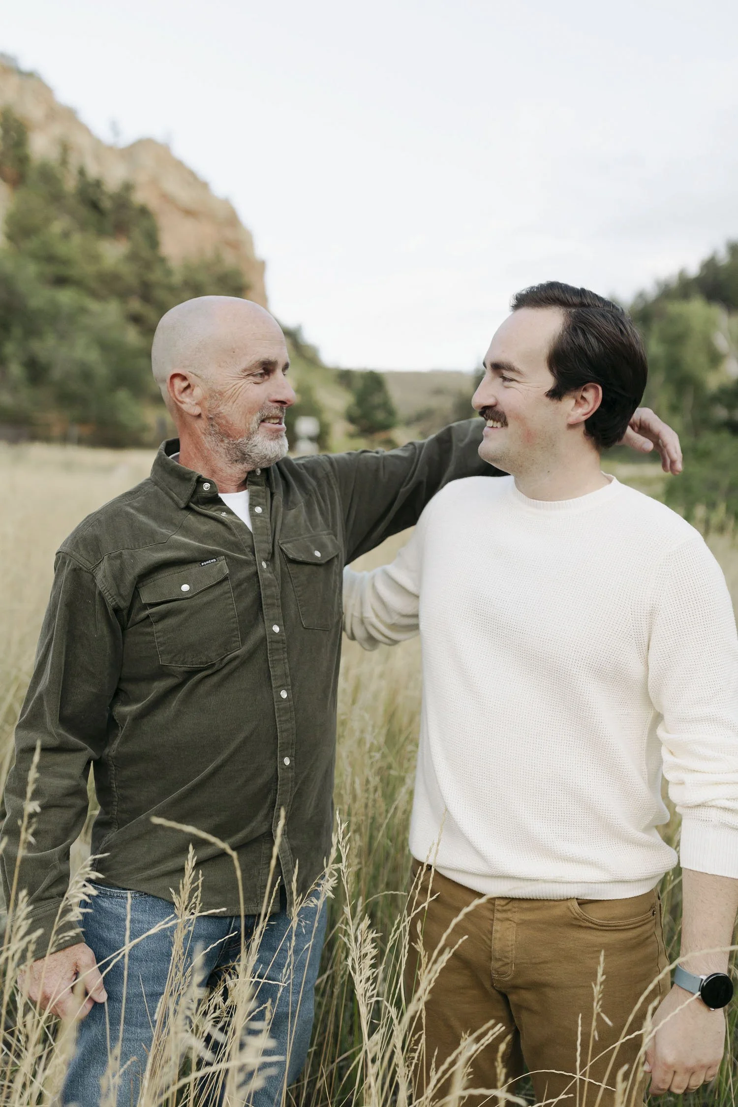 Outdoor portrait of father and son standing together in a field, sharing a warm, relaxed moment in nature.