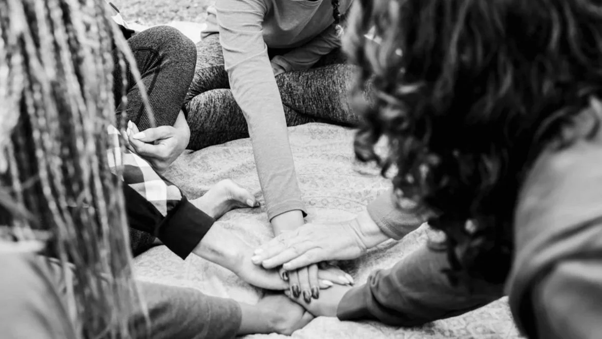 Group of people sitting together with hands joined in the center, reflecting connection, support, and shared presence