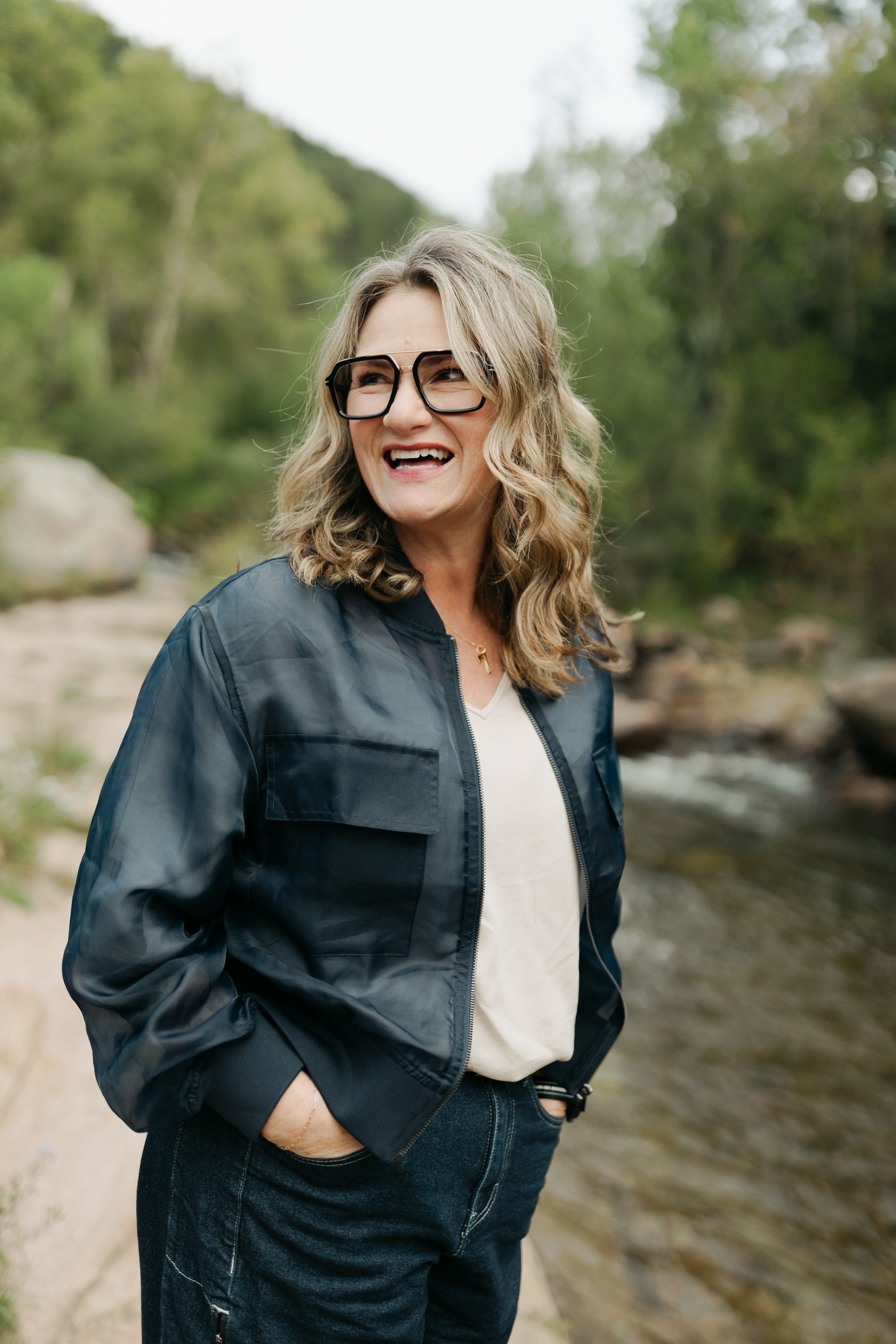 Portrait of Jill Krush standing by the river, smiling and relaxed, representing her grounded and relational approach to healing.