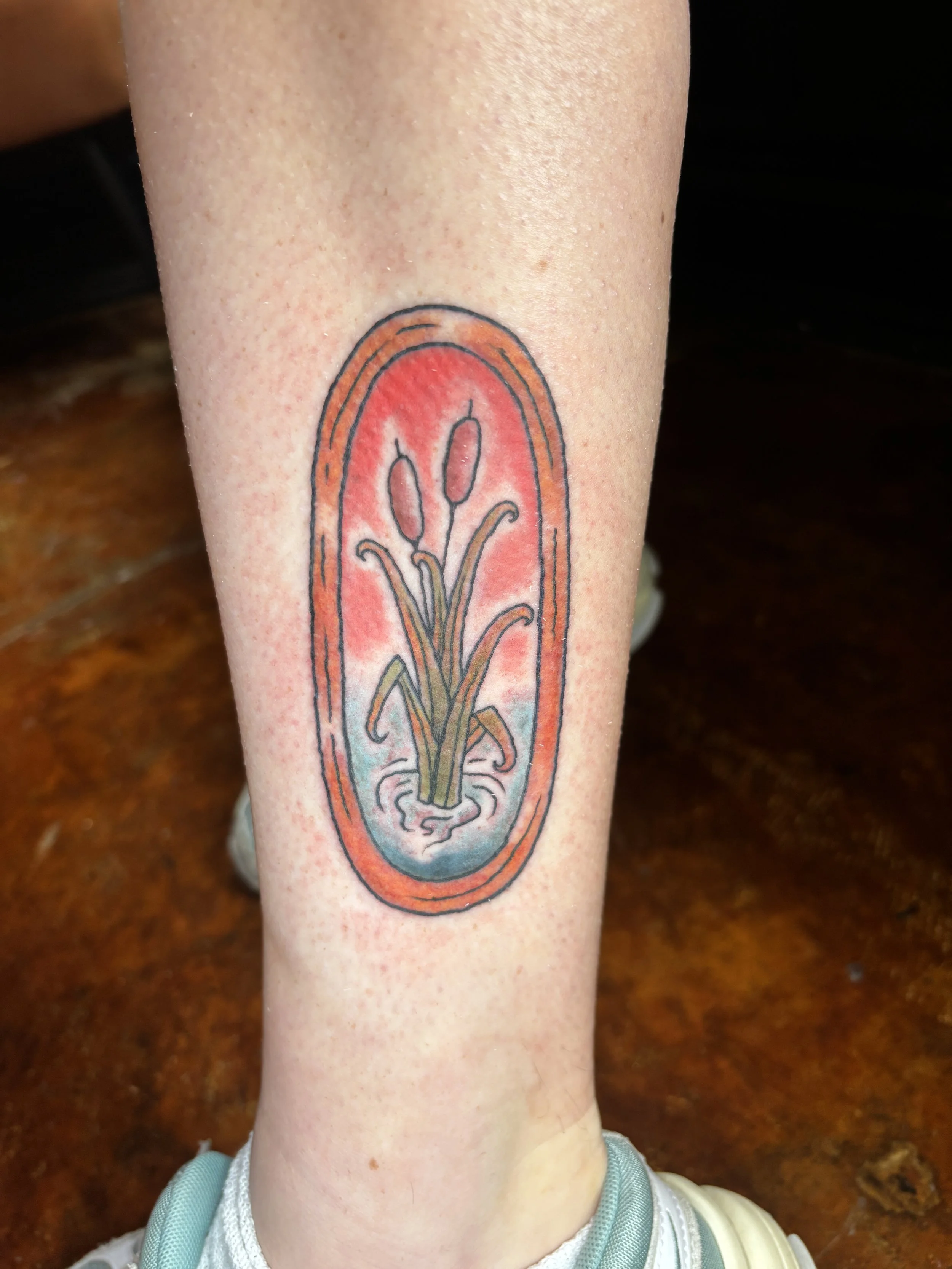 A tattoo on a person's arm depicting a stylized plant or sprout inside an elongated, oval-shaped frame with red and orange hues.