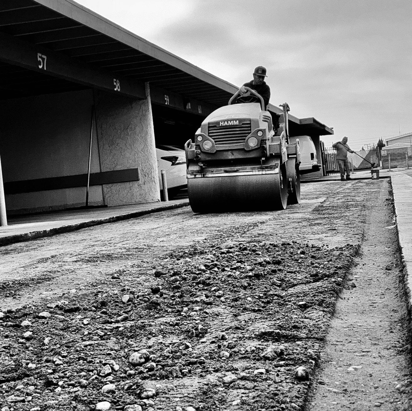 A worker operating a road roller compactor on a construction site near a parking. setting grade and compaction for asphalt repair