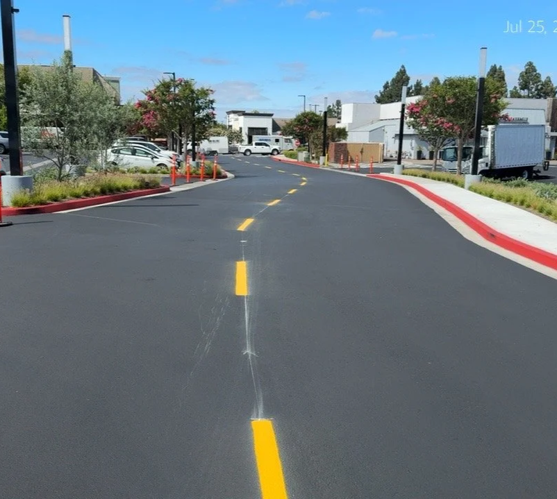 Empty parking lot with newly paved and seal coasted asphalt , yellow dotted street lines, painted red curbs, and vehicles in the background on a sunny day. Irvine California orange county