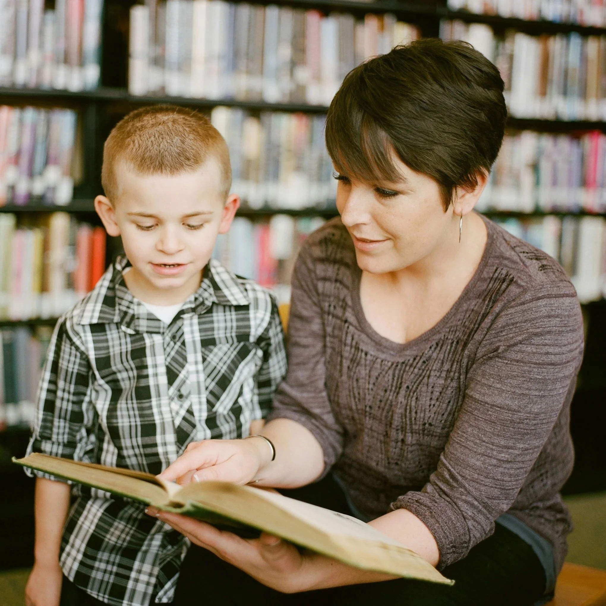 A woman reading a book with a young boy in a library.